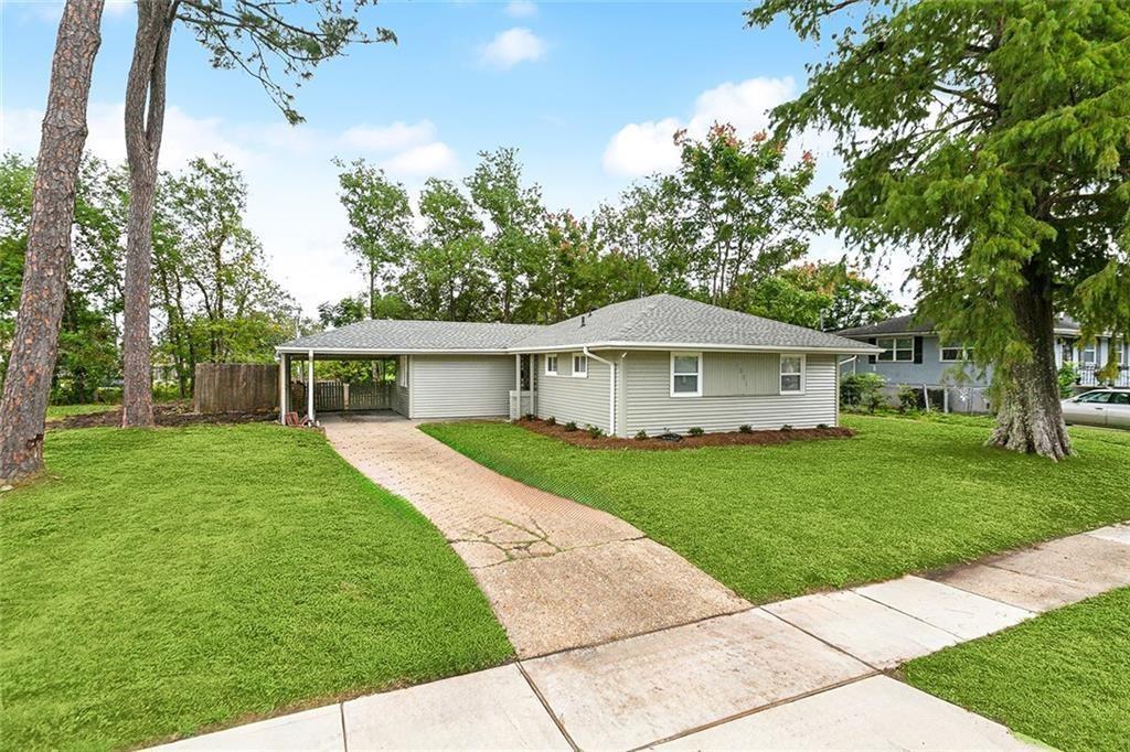 Single-story house with an attached carport, broad lawn, and mature trees.