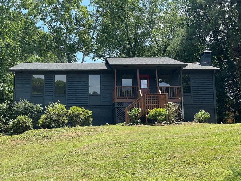 Single-story dark blue-gray house with a raised wooden porch and steps on a grassy slope.