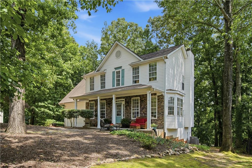 White two-story house with a stone-clad lower facade and covered patio in a wooded yard.