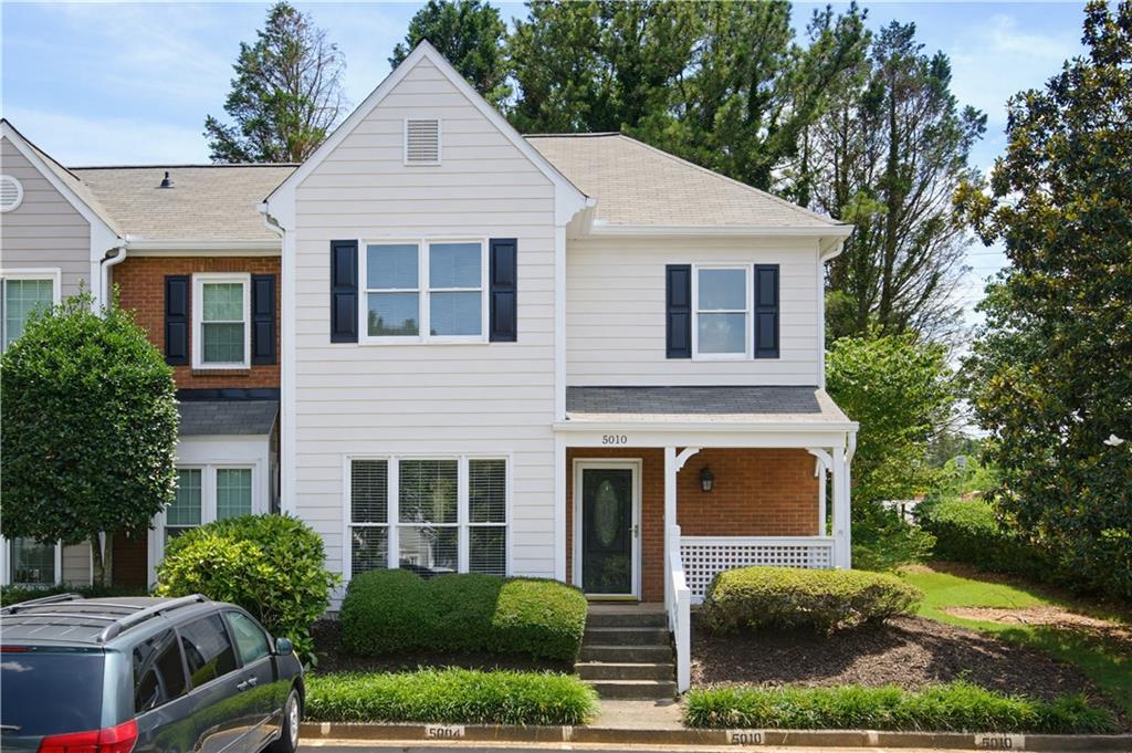 White-sided townhouse with a brick entry, covered porch, and landscaped shrubs.