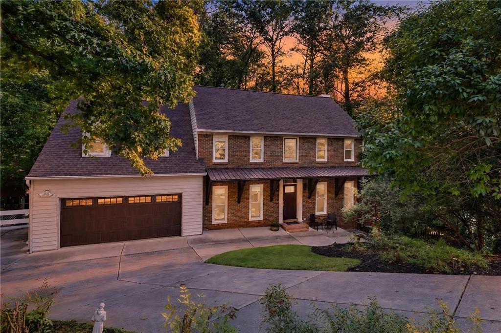 Two-story brick house with an attached garage and covered front porch, framed by mature trees.