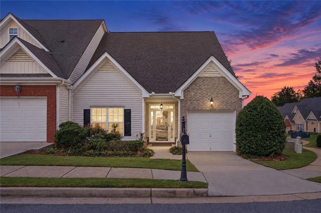Suburban home with cream siding, brick accents, and two garage doors beneath a colorful dusk sky.