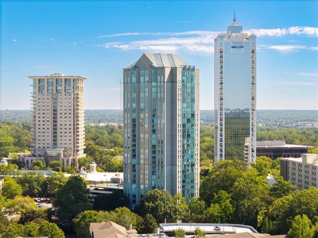 Three high-rise buildings rise above a leafy city landscape beneath a blue sky.