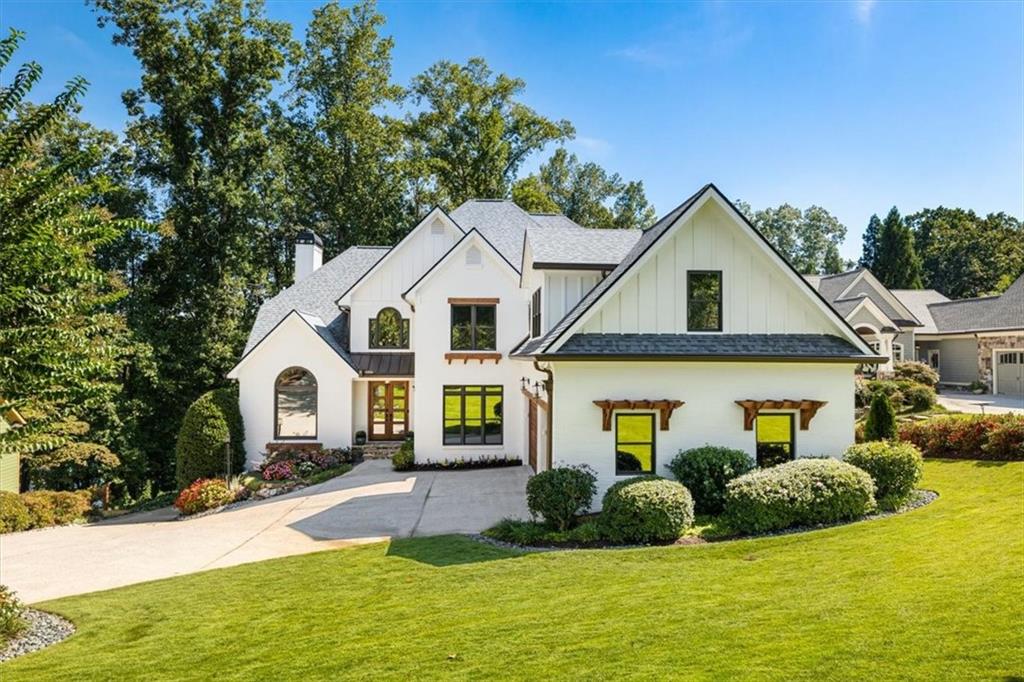 White two-story house with varied gables, an arched window, landscaped shrubs, and a broad driveway.