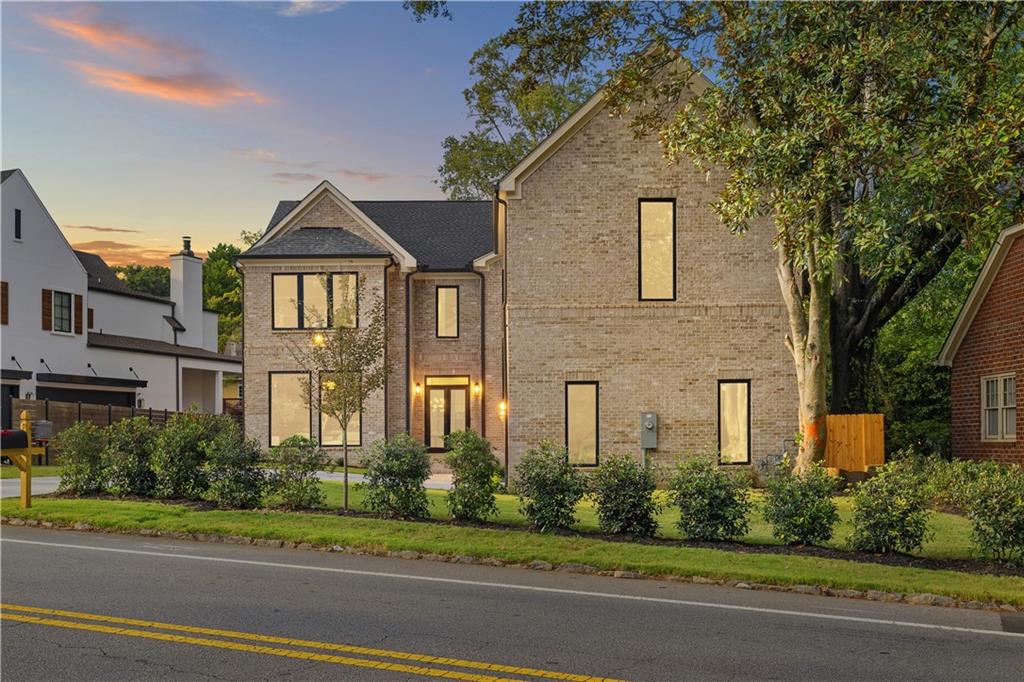 Two-story brick home with a landscaped front yard and glowing windows at sunset.