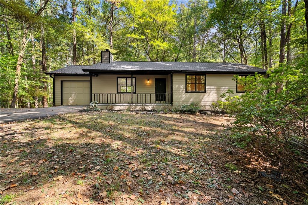Single-story home with a covered porch and attached garage surrounded by mature trees.