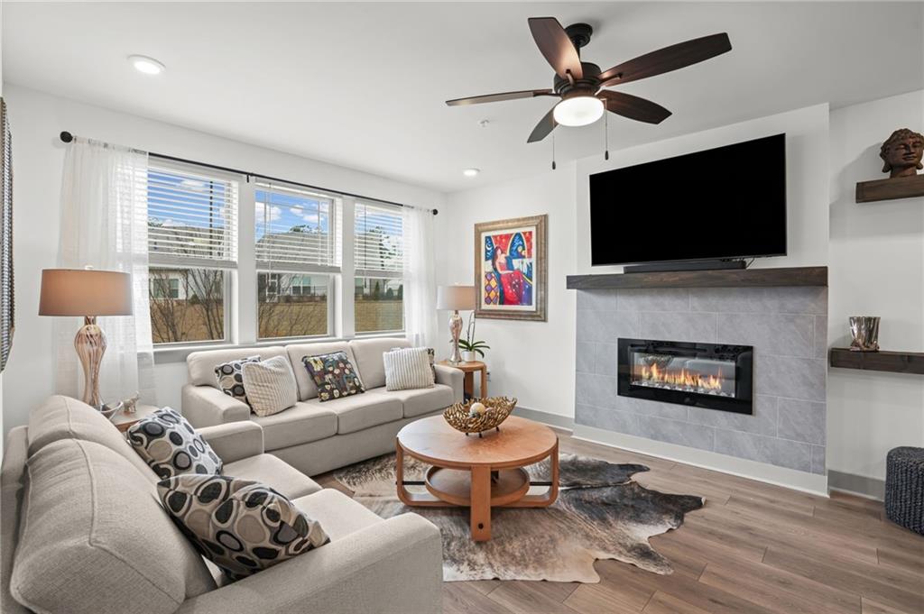 Bright living room with a sectional sofa, tiled fireplace, wall-mounted TV, and wide windows.
