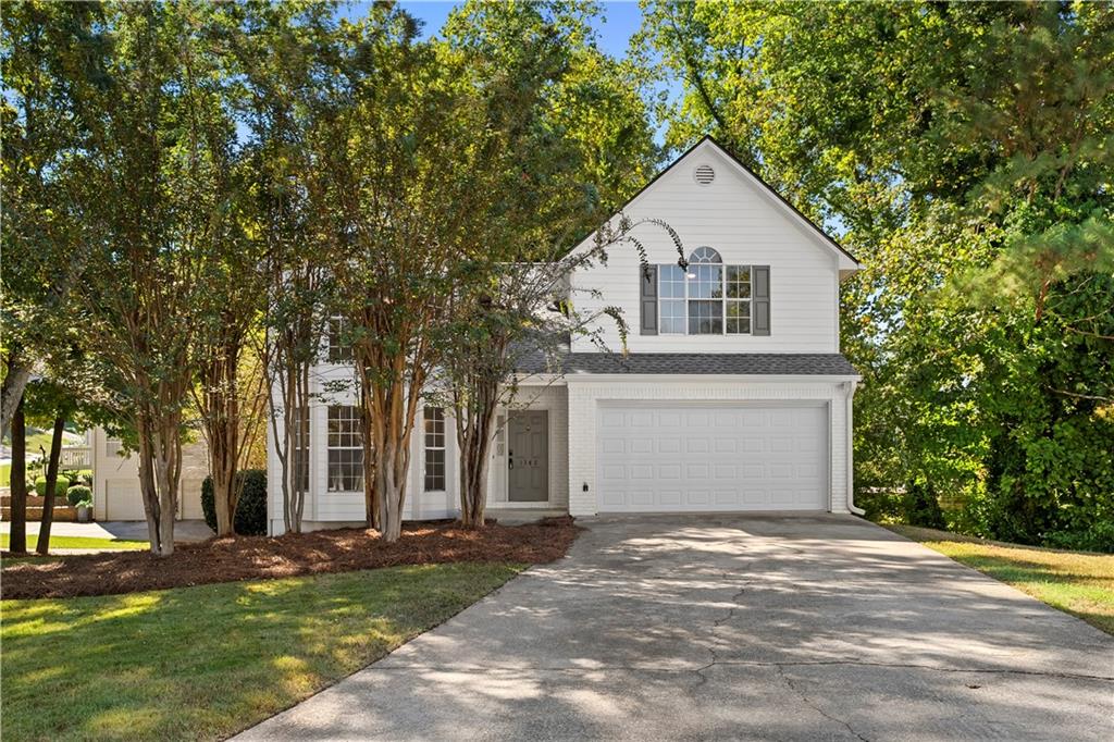 White two-story home with a double garage, wide driveway, and mature trees.