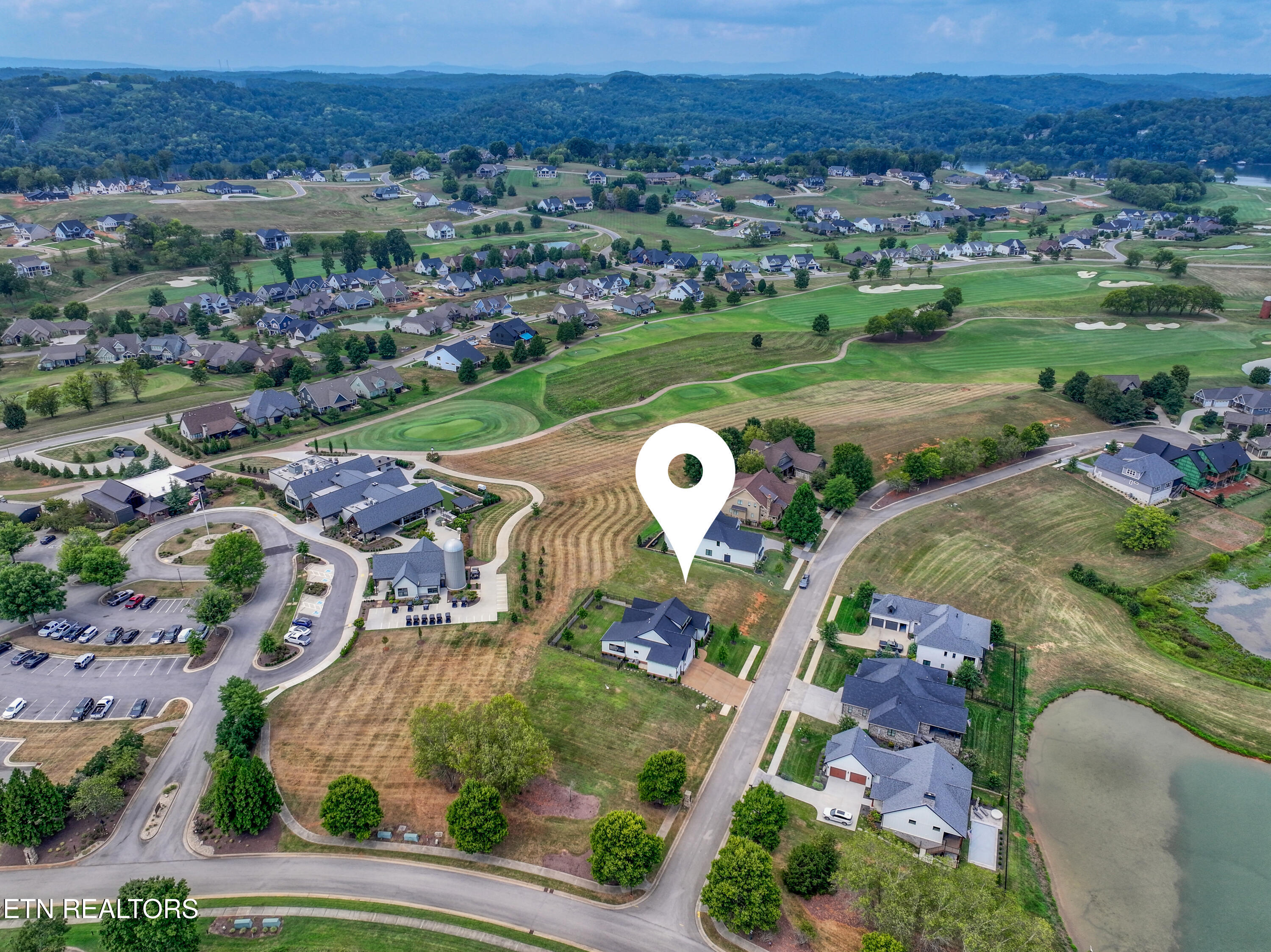 Aerial view of a home site beside a golf course, with neighborhood and pond.