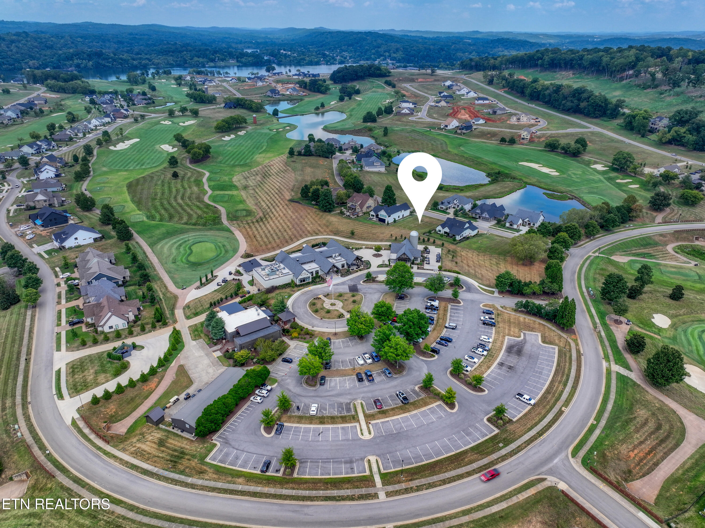 Aerial view of homes beside a golf course and ponds, with a location pin marking a home.