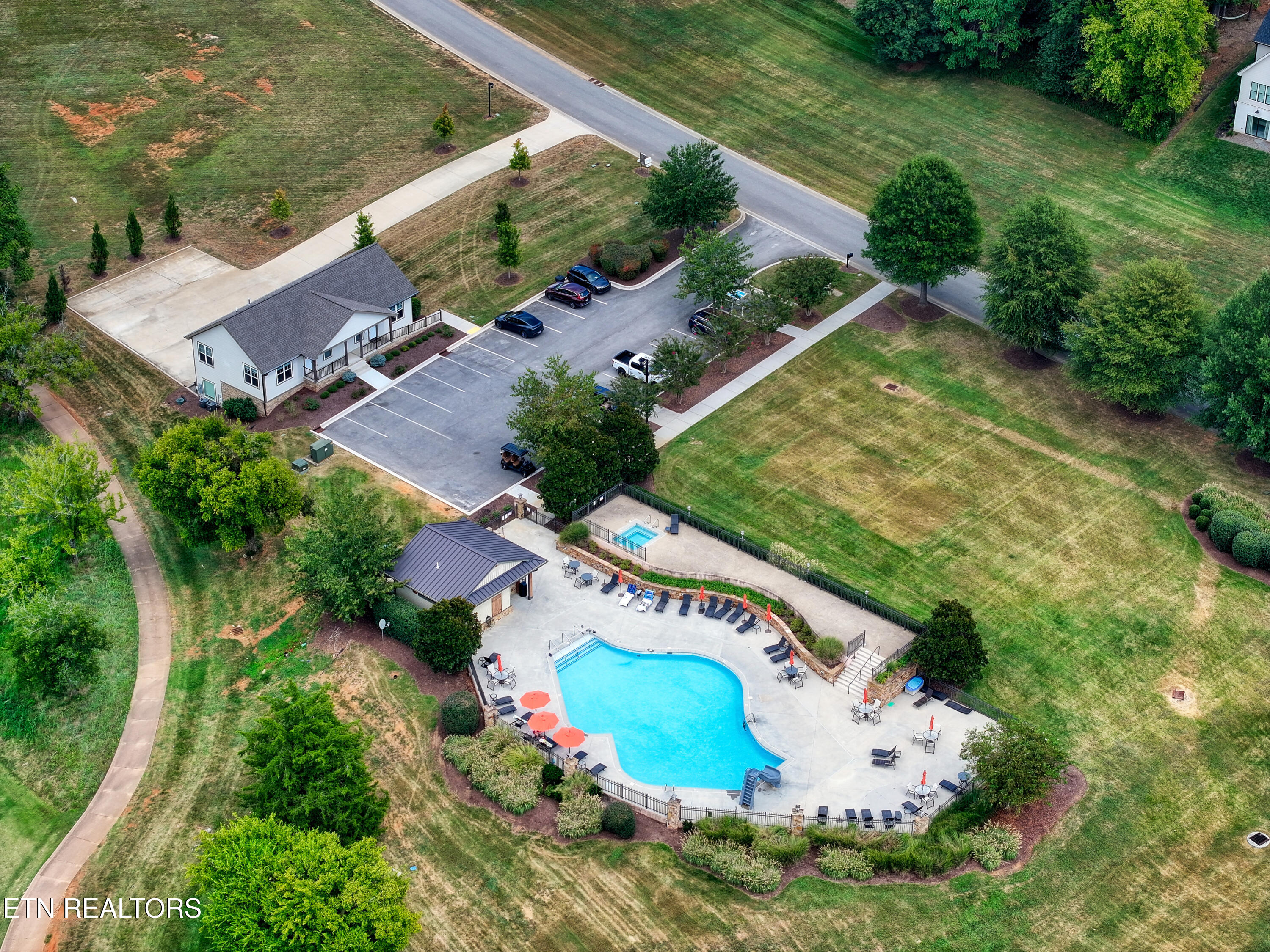 Aerial view of a community pool, clubhouse, parking lot, and landscaped grounds.