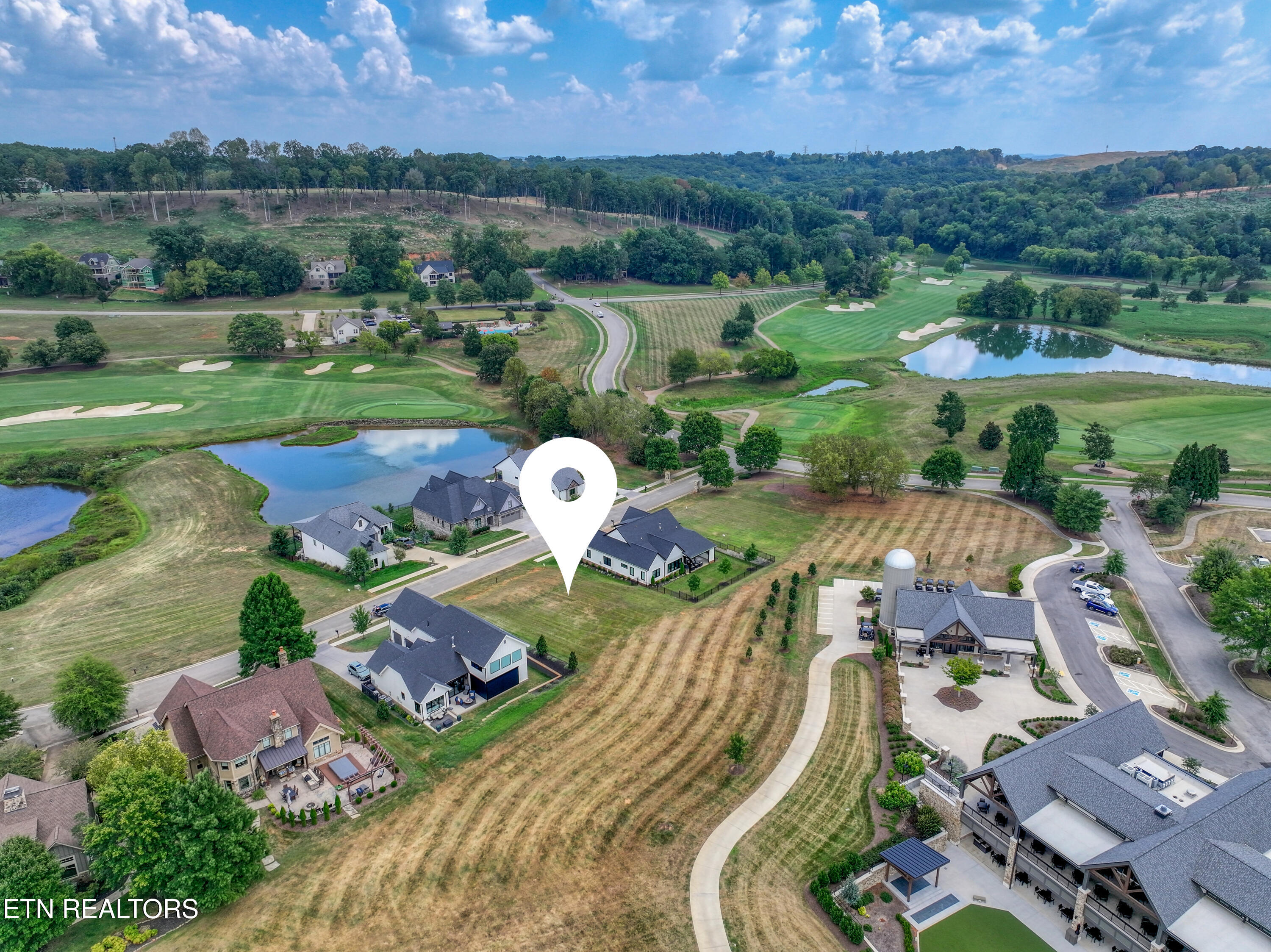 Aerial view of a home marked by a pin among a golf course community, ponds, and clubhouse.