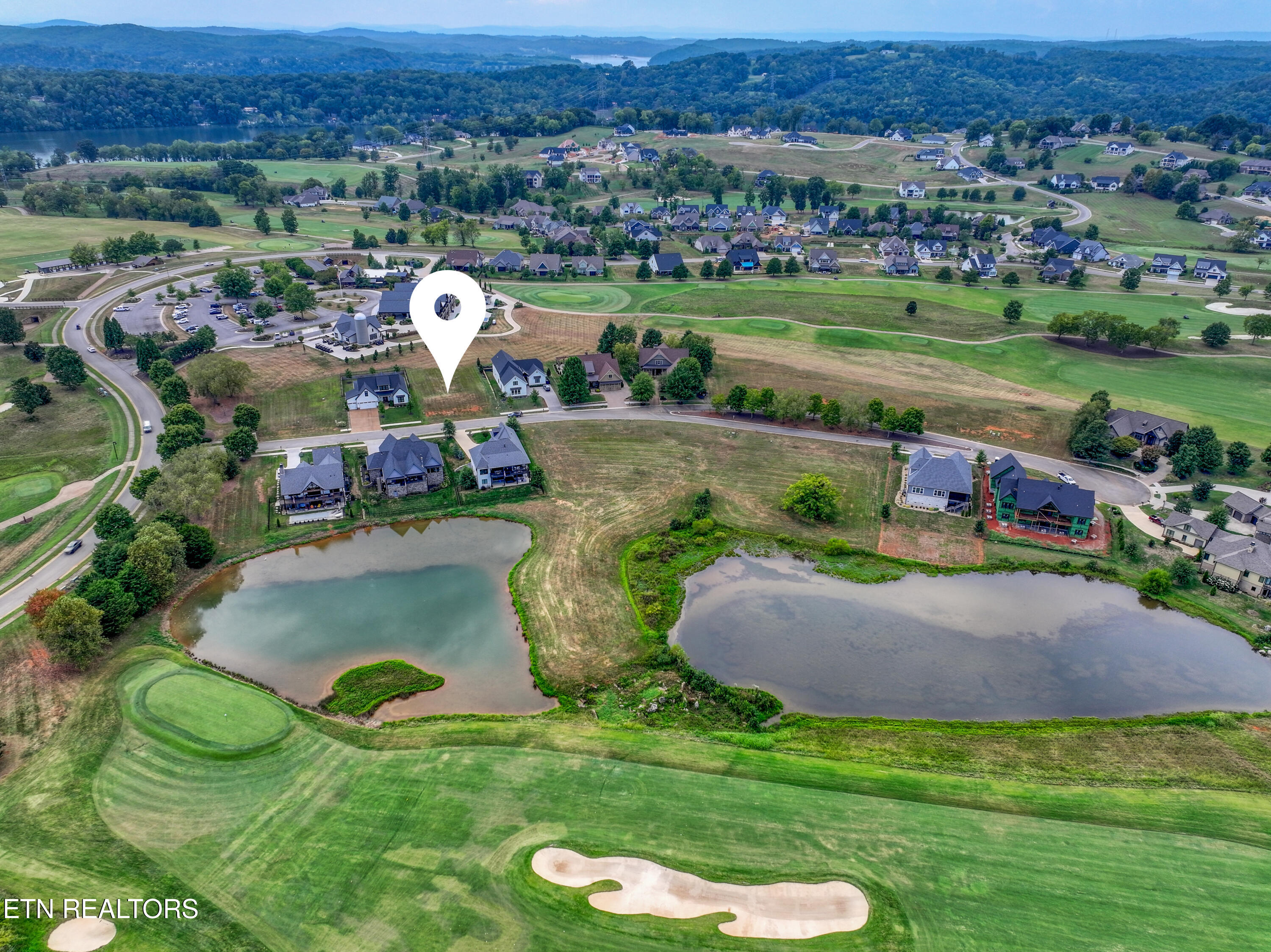Aerial view of a marked homesite beside golf course fairways and ponds in a residential community.
