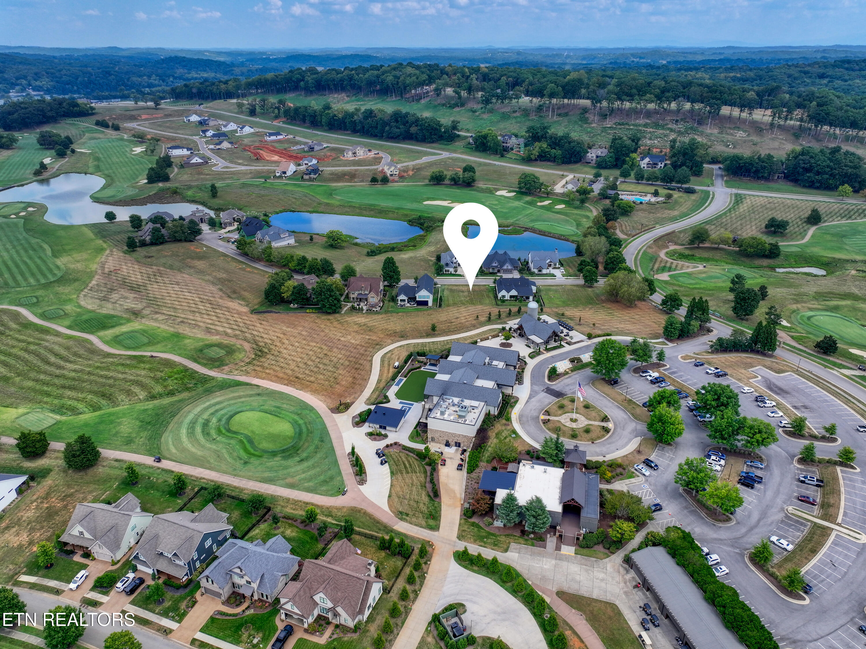 Aerial view of homes beside a golf course and ponds, with a map pin marking the property.