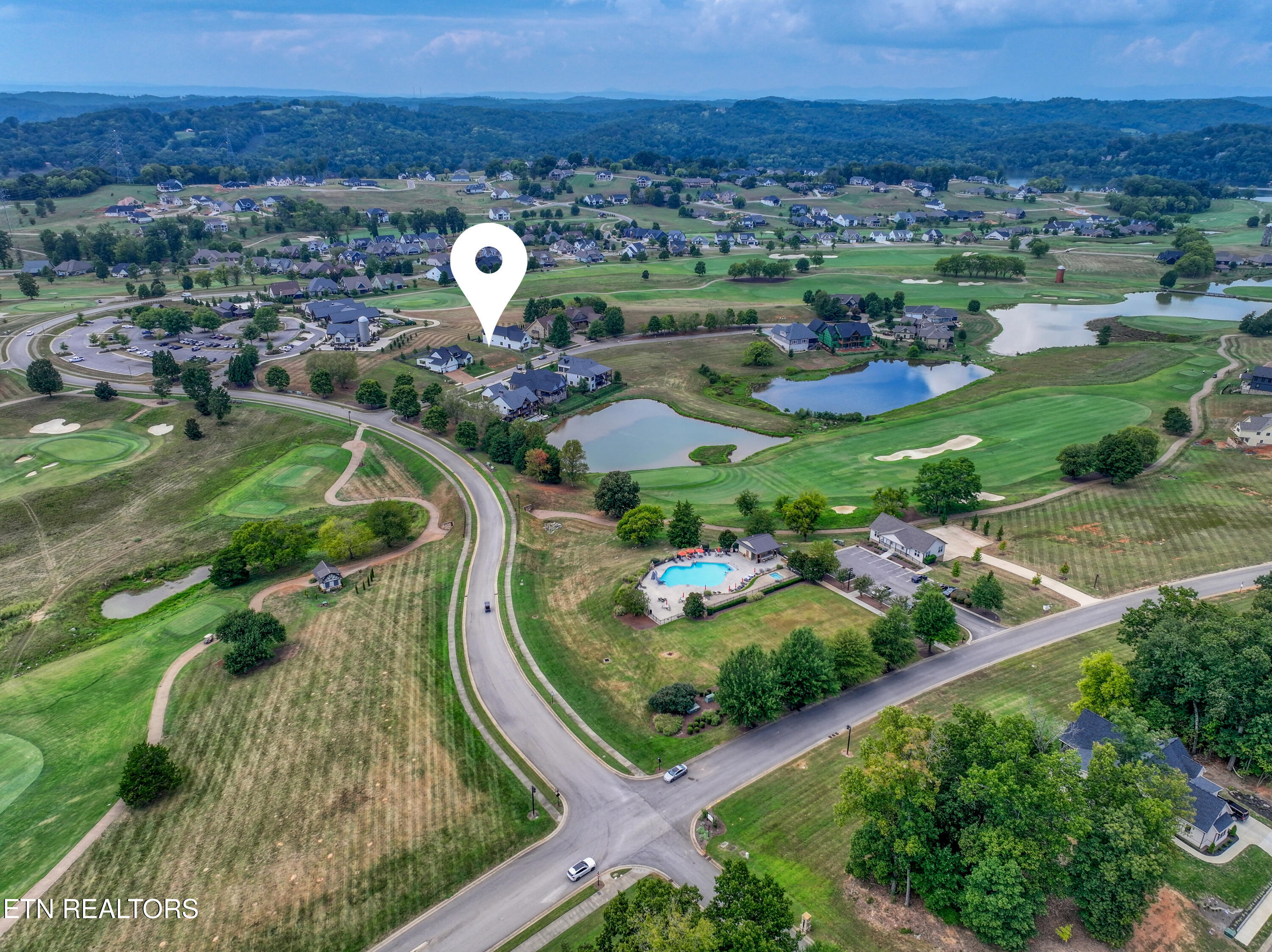 Aerial view of a home marked by a map pin amid a golf course, ponds, and neighborhood homes.