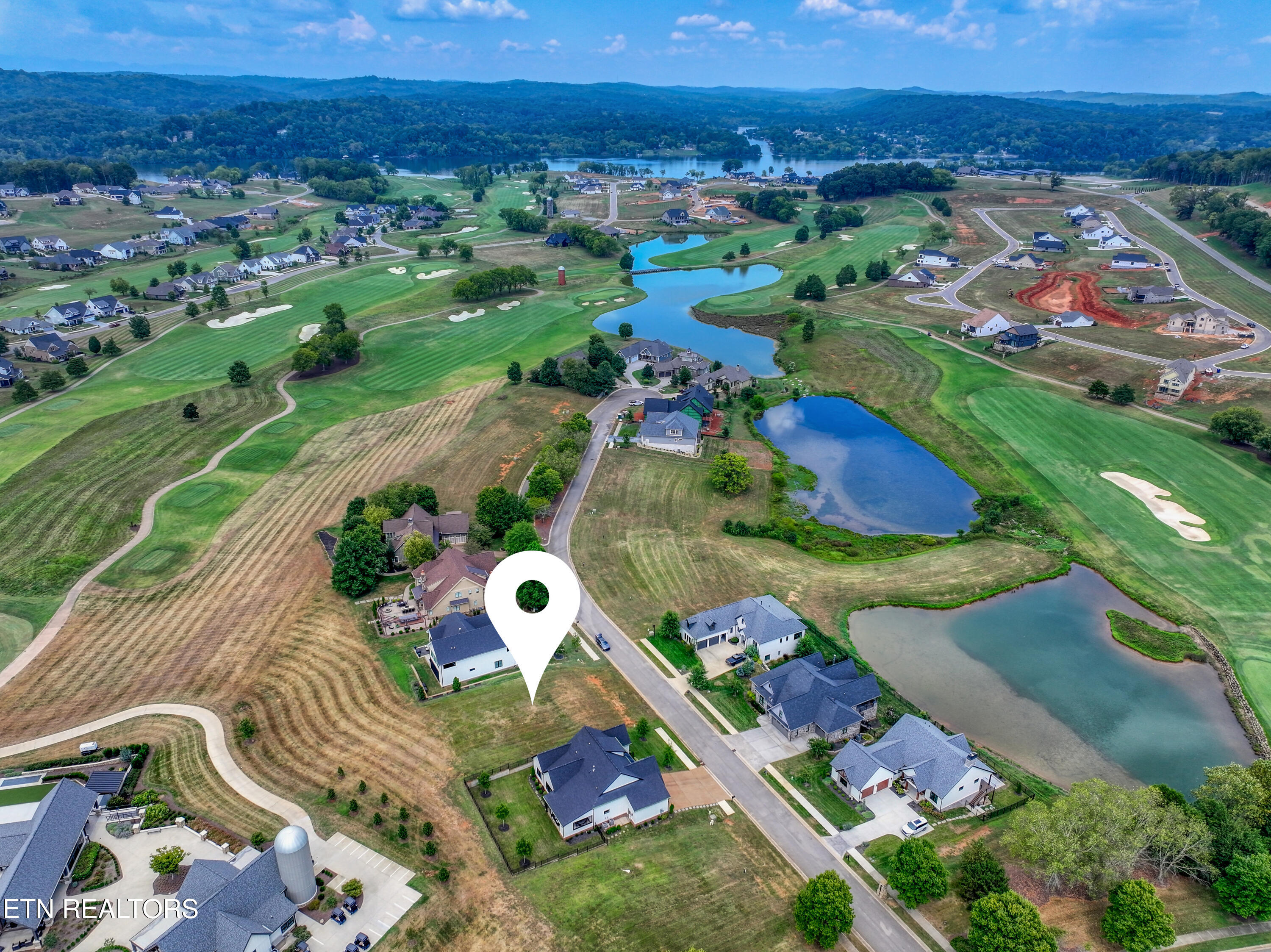 Aerial view of a vacant lot marked by a pin beside homes, ponds, and a golf course.