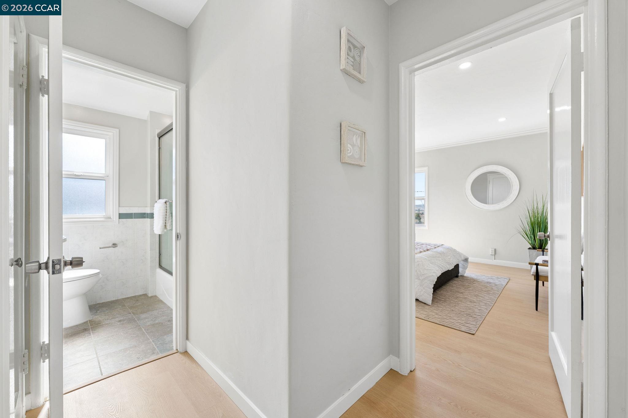 Hallway with a tiled bathroom on one side and a furnished bedroom on the other.