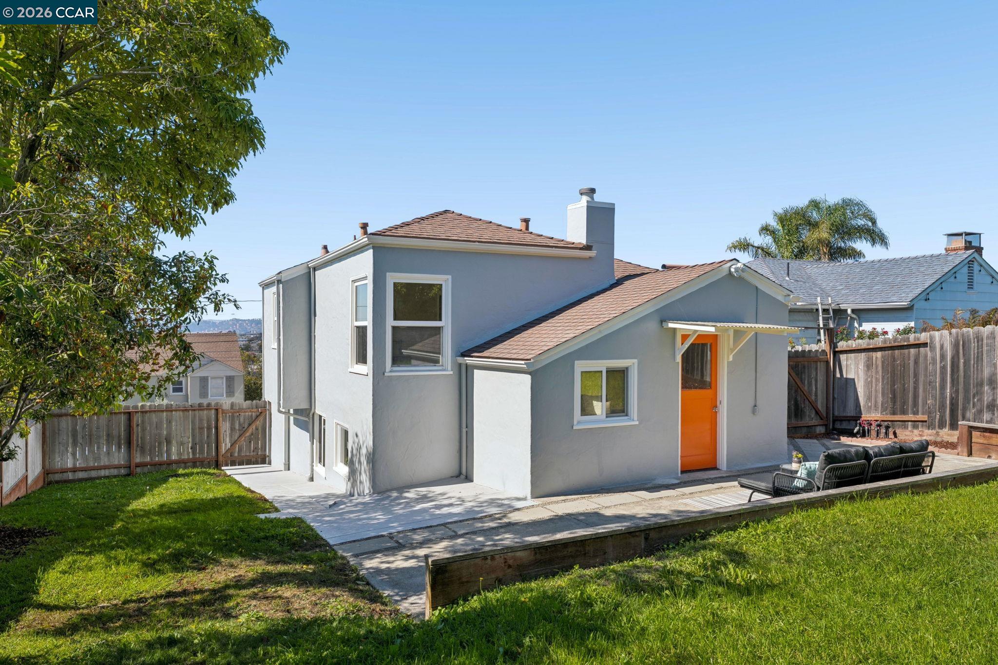 Gray two-story home with an orange door and fenced backyard patio.