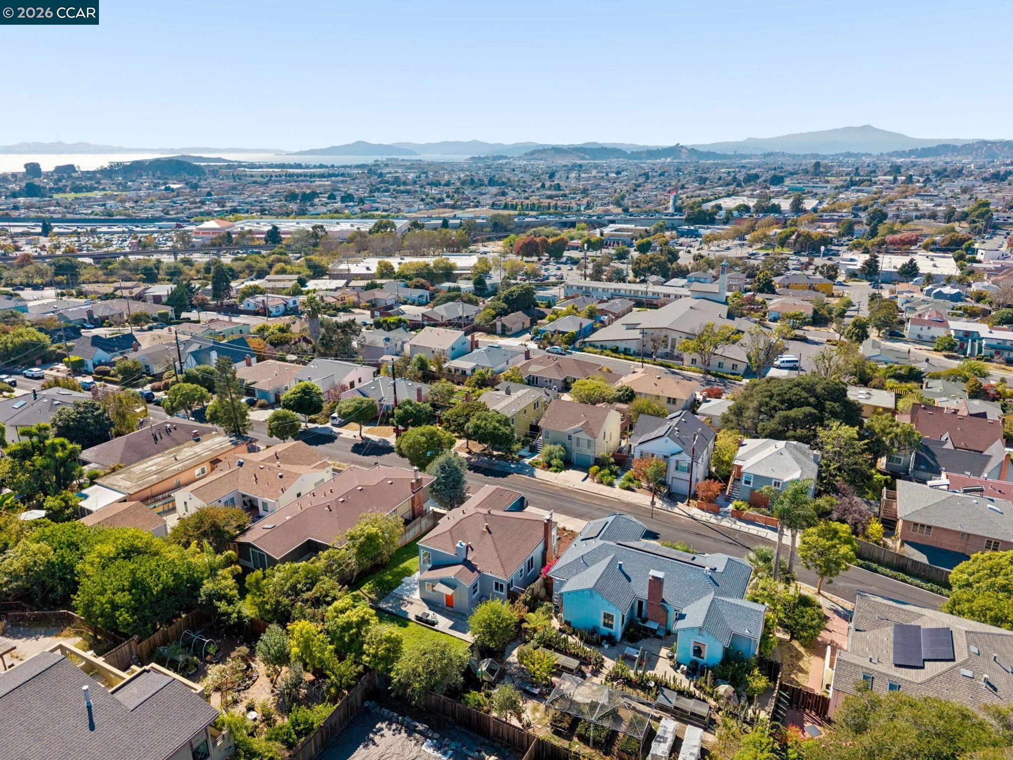 Aerial view over the home and surrounding neighborhood, with the bay and hills in the distance.