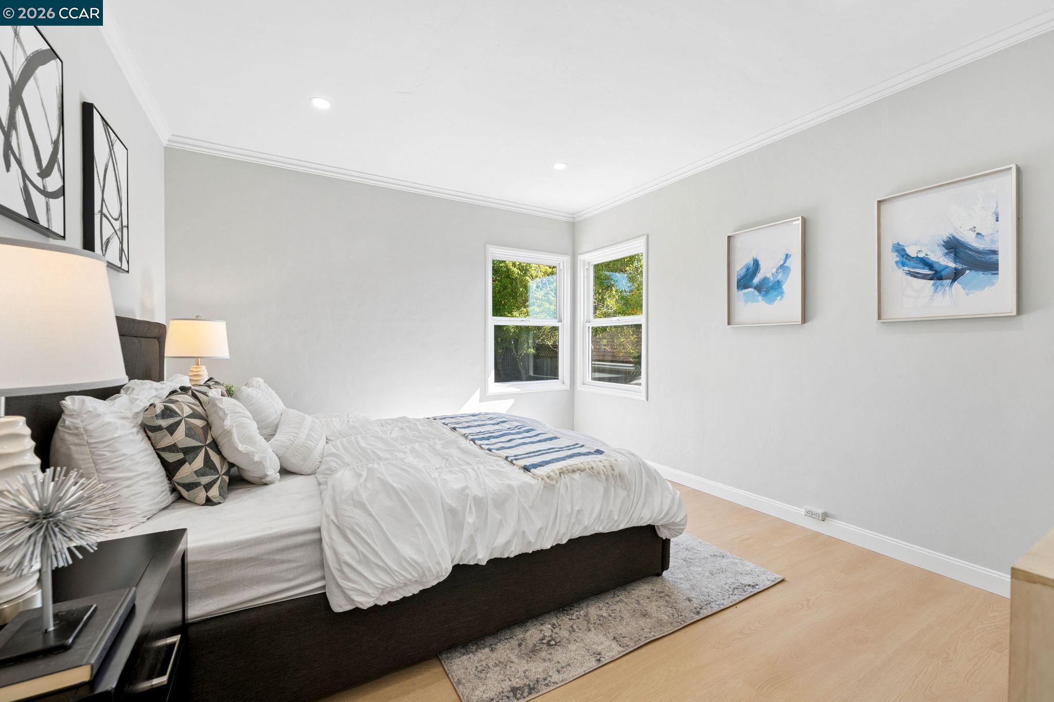 Staged bedroom with a dark bed, white bedding, blue-striped throw, and two windows overlooking trees.