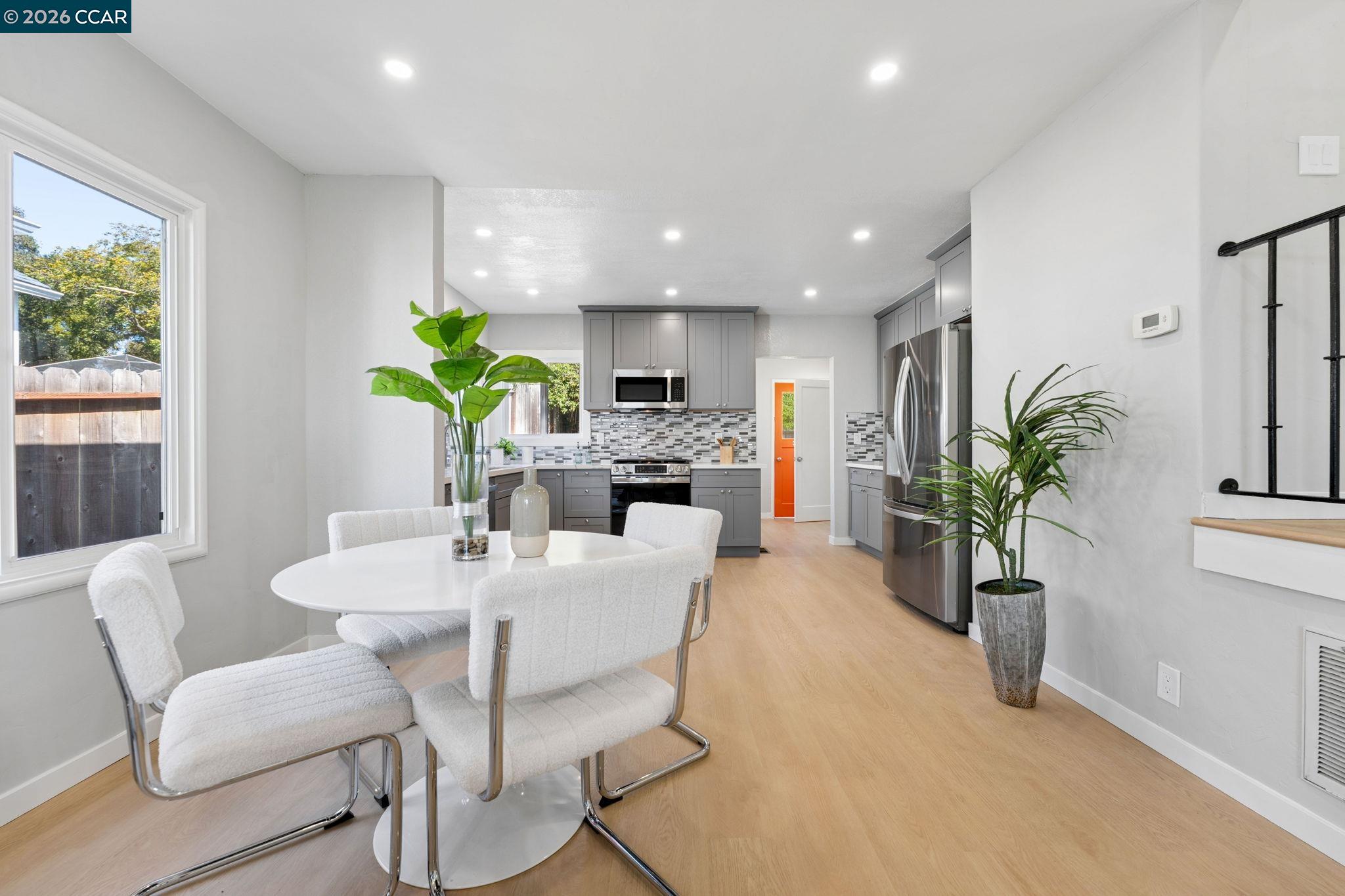 Open-plan kitchen and dining area with gray cabinets, stainless steel appliances, and a white round table by the window.
