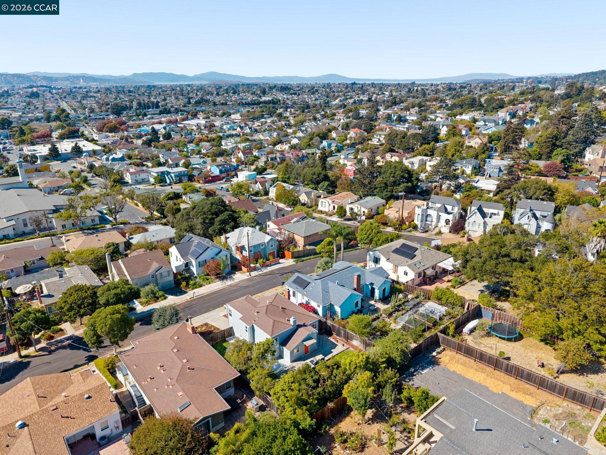 Aerial view of a residential neighborhood with tree-lined streets and distant hills.