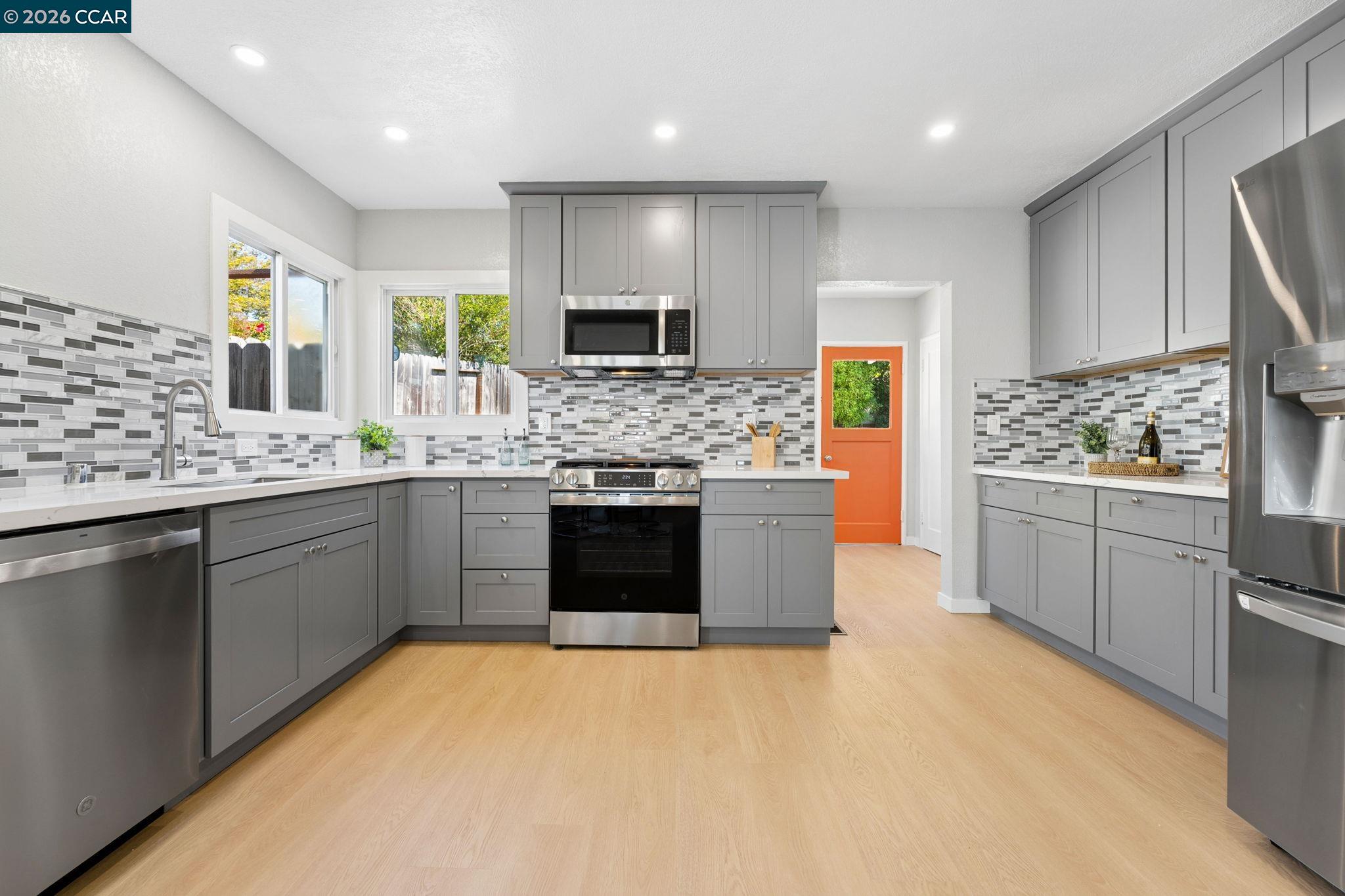 Remodeled kitchen with gray cabinets, mosaic tile backsplashes, stainless appliances, and an orange back door.