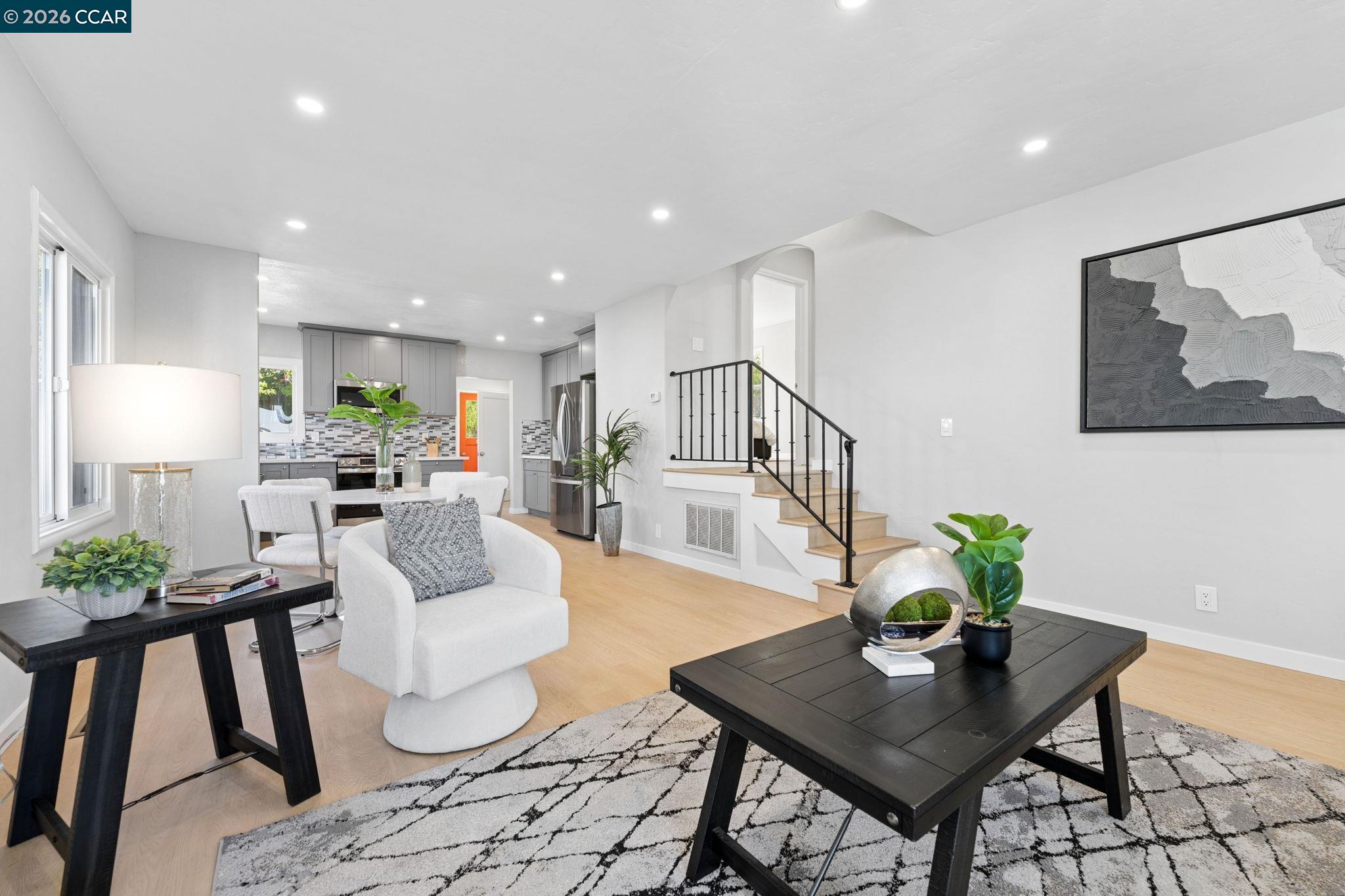 Open-plan living room with a white armchair, black coffee table, and adjoining gray kitchen.