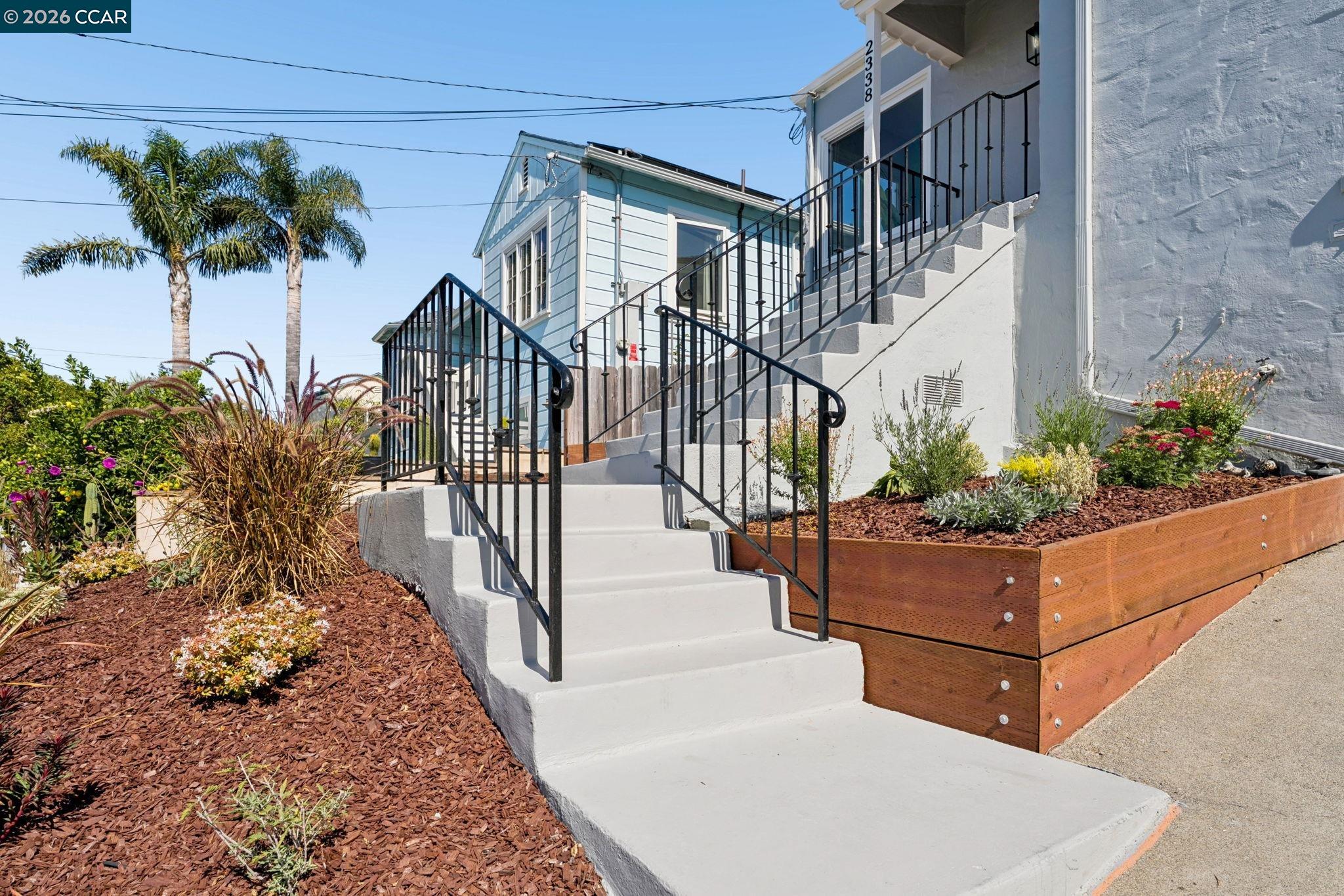 Home entrance with broad concrete steps, black railings, and landscaped garden beds.