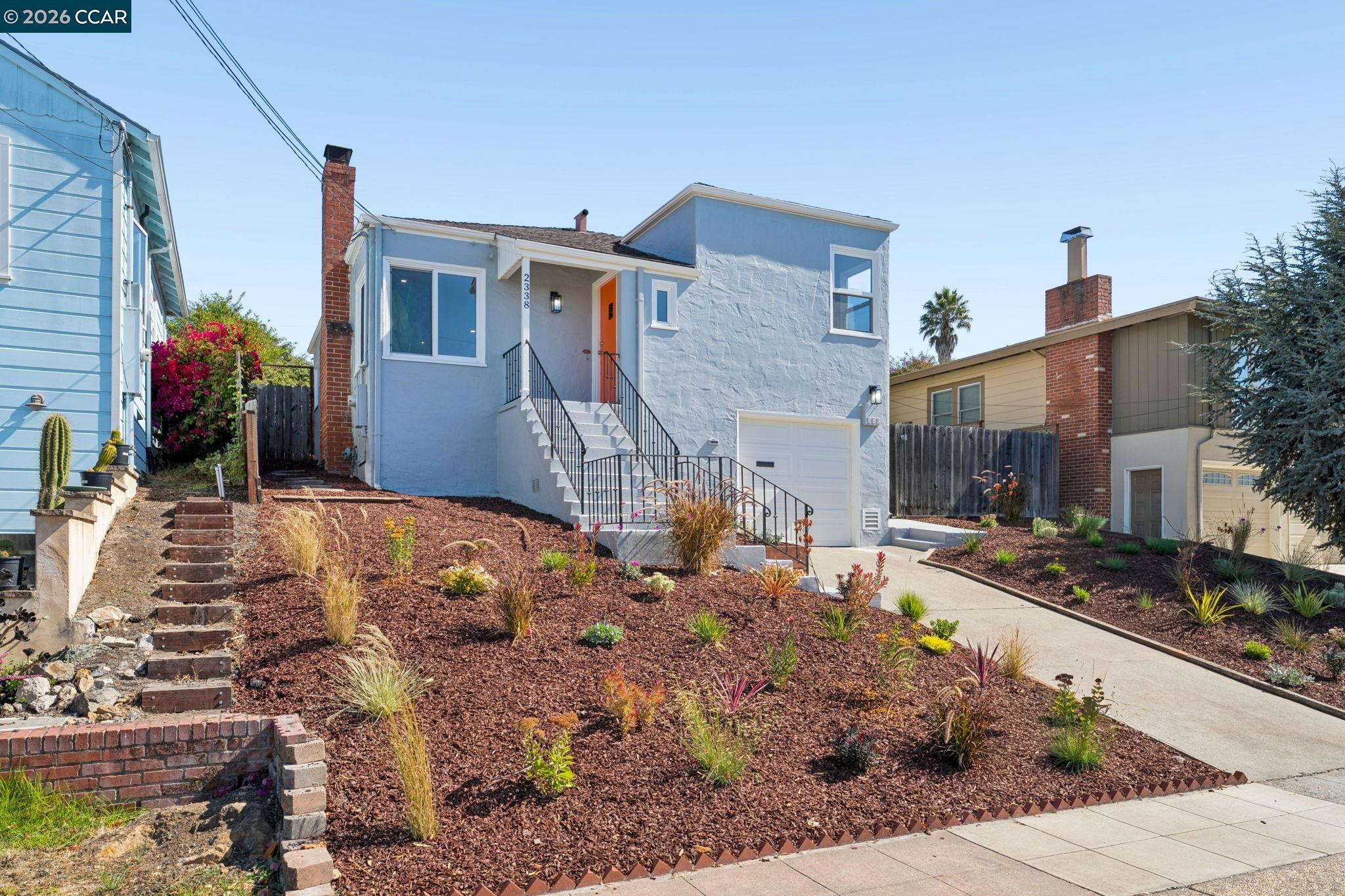 Light-blue house with an orange front door, raised entry stairs, and landscaped front yard.