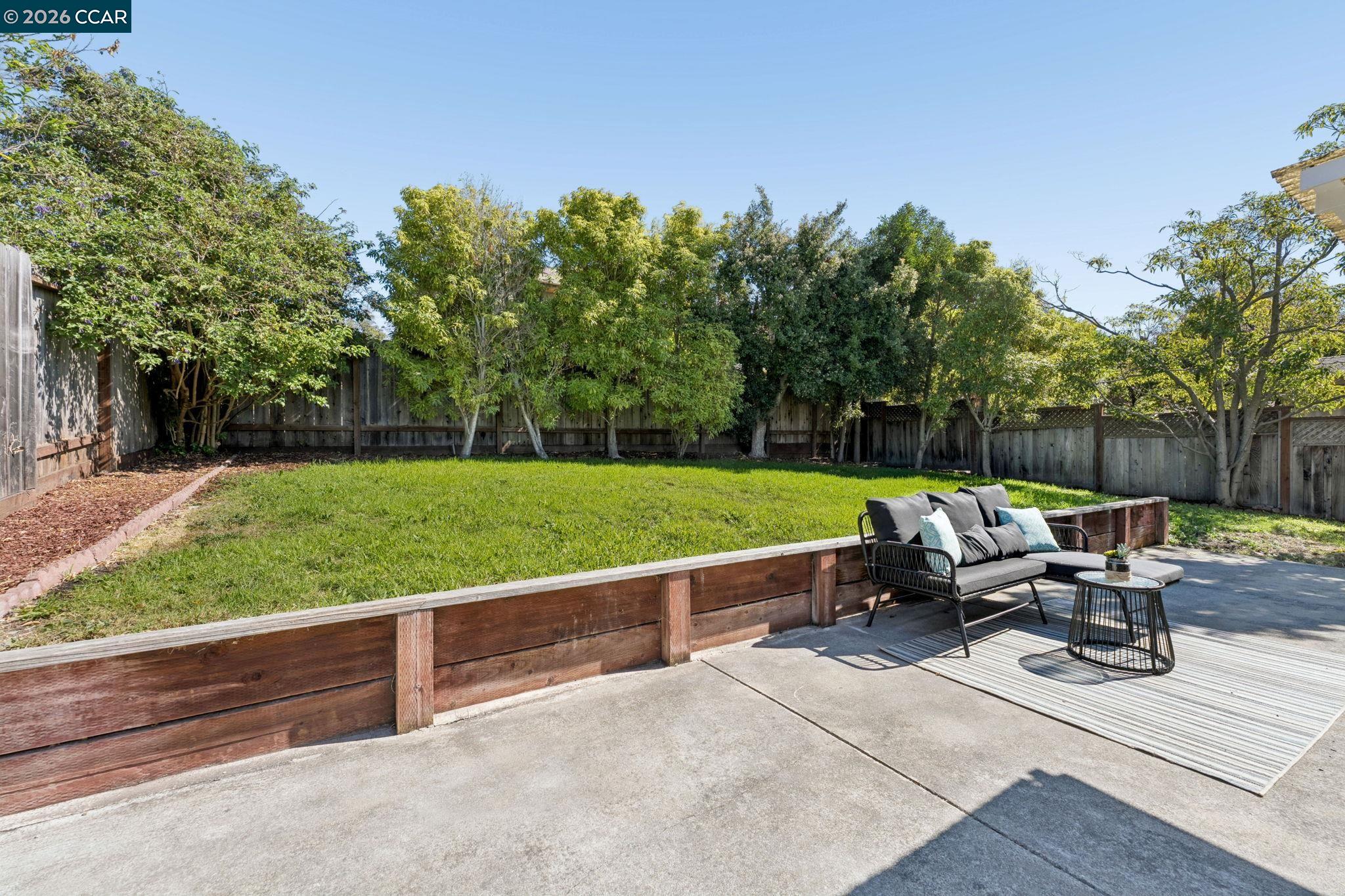 Backyard patio with a raised lawn, mature trees, and cushioned outdoor seating.