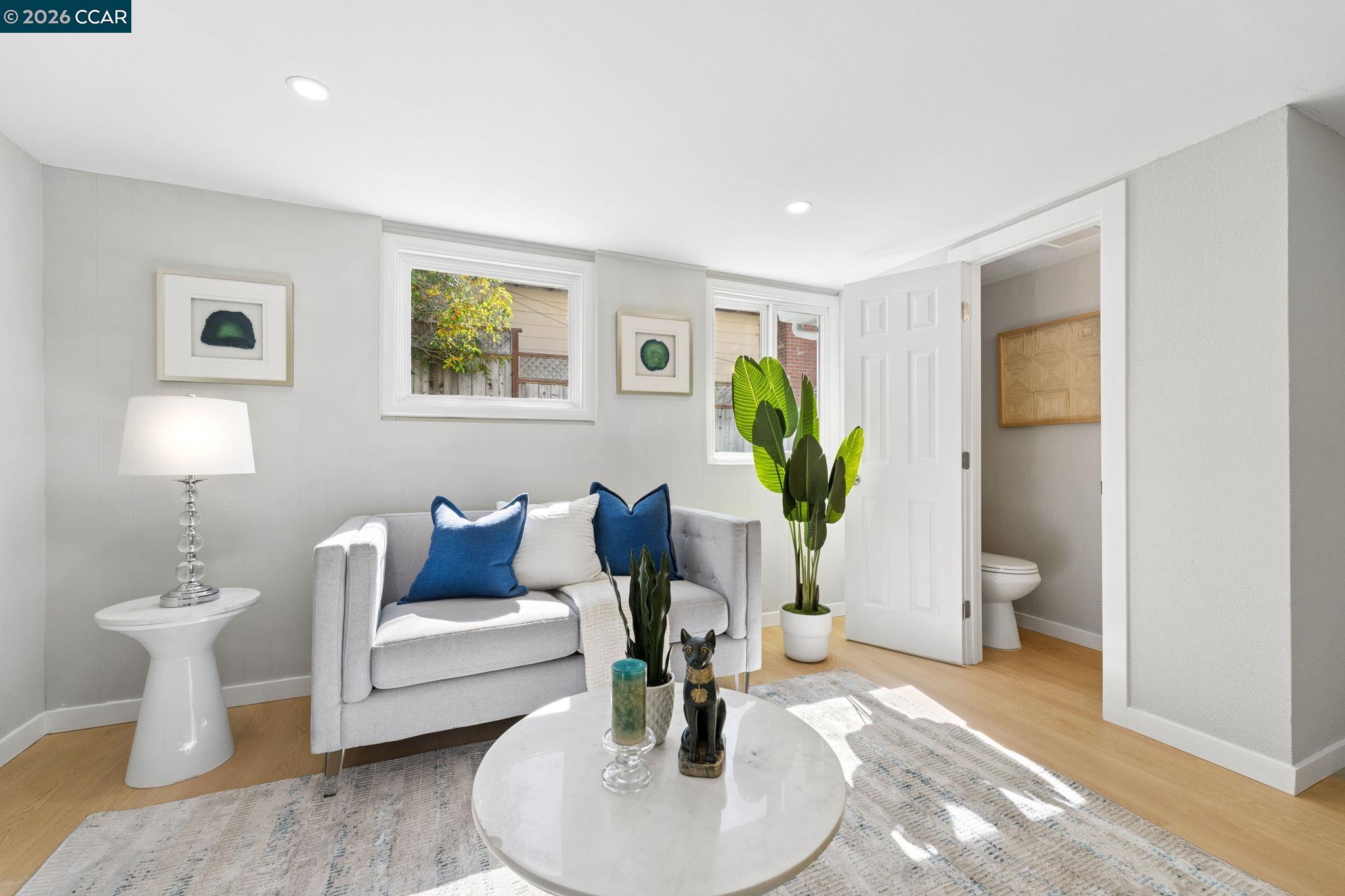 Staged sitting room with a gray sofa, blue cushions, round coffee table, and an open view into the bathroom.