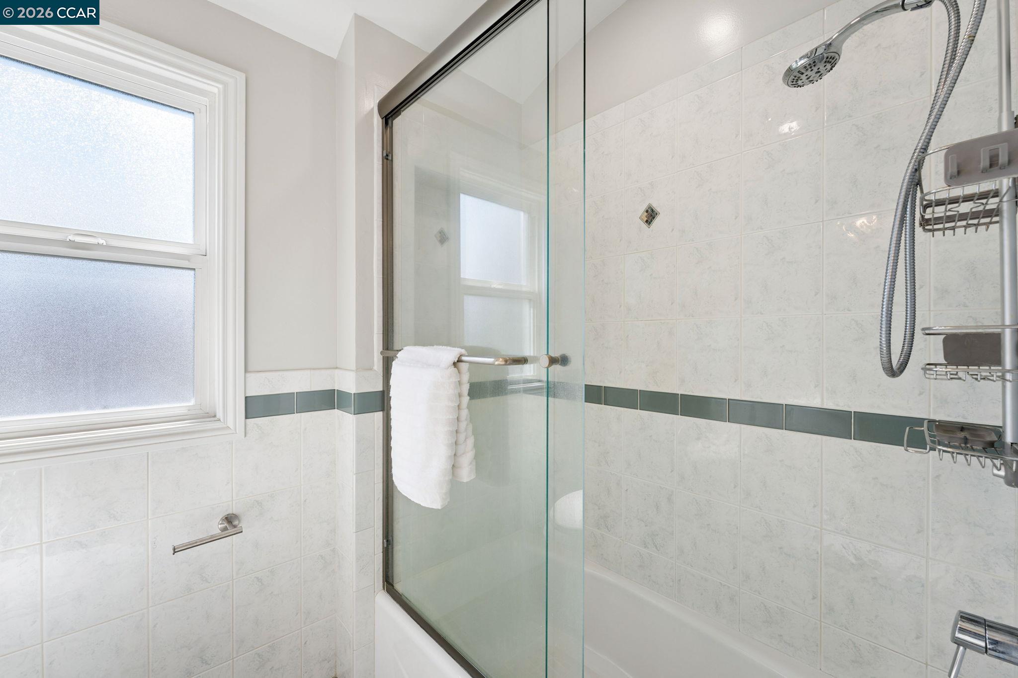 Tiled bathroom with a glass shower enclosure, frosted window, and white towels.