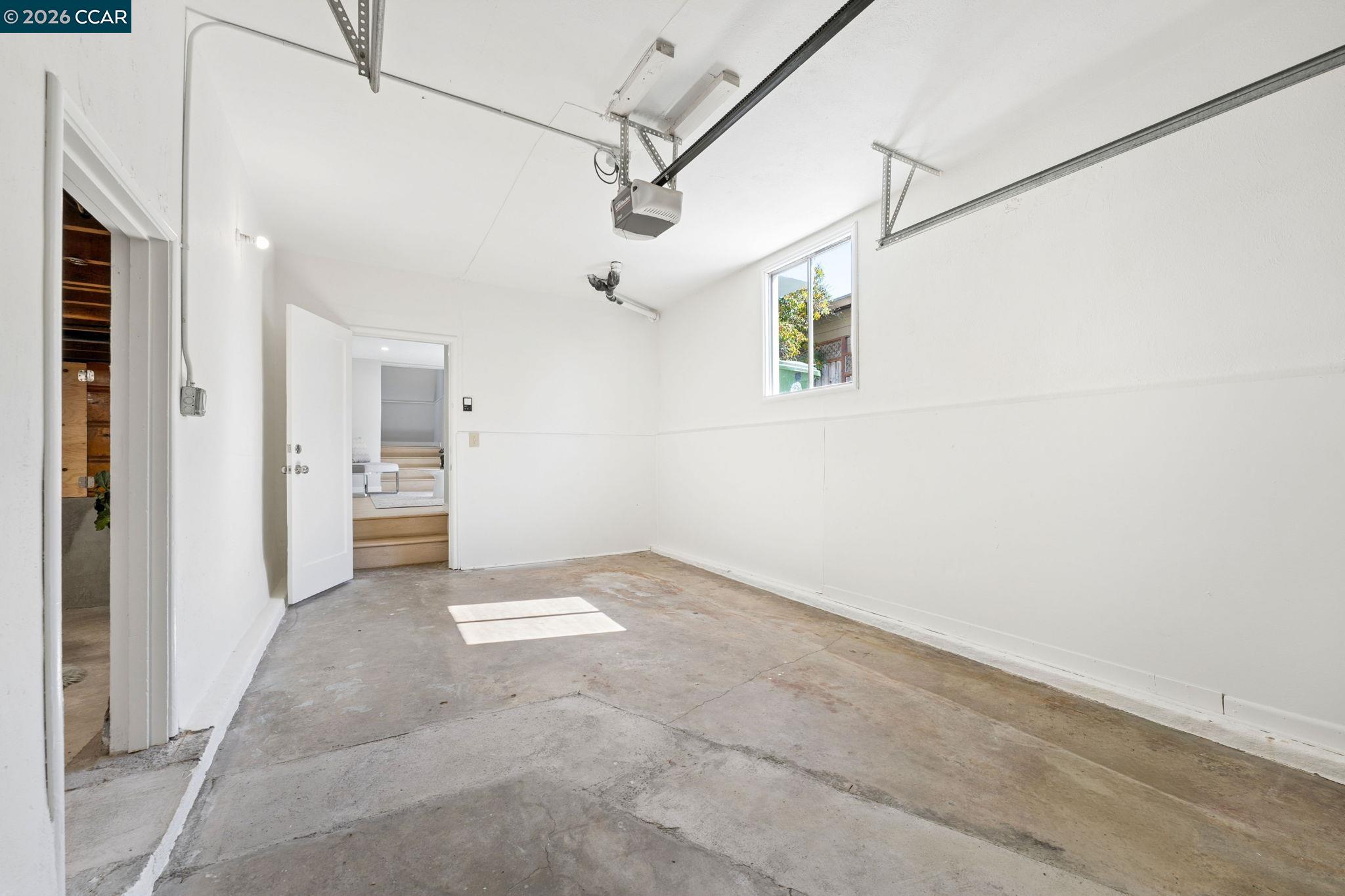 Empty garage with a concrete floor, overhead door tracks, and sunlight through a small window.