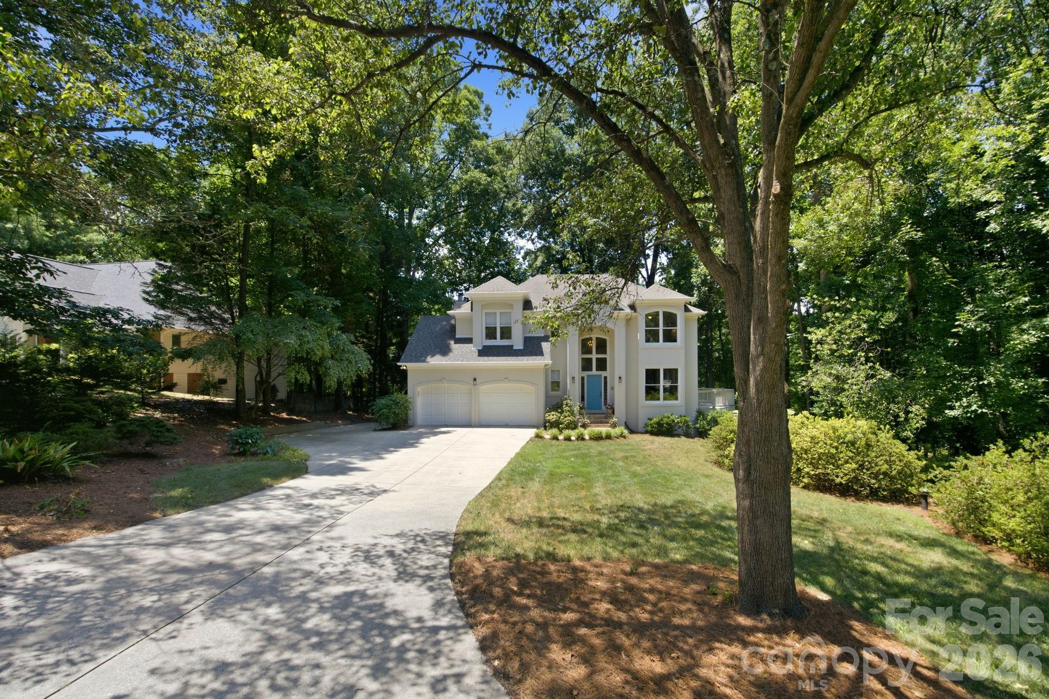 Two-story home with a blue front door and double garage, framed by mature trees.