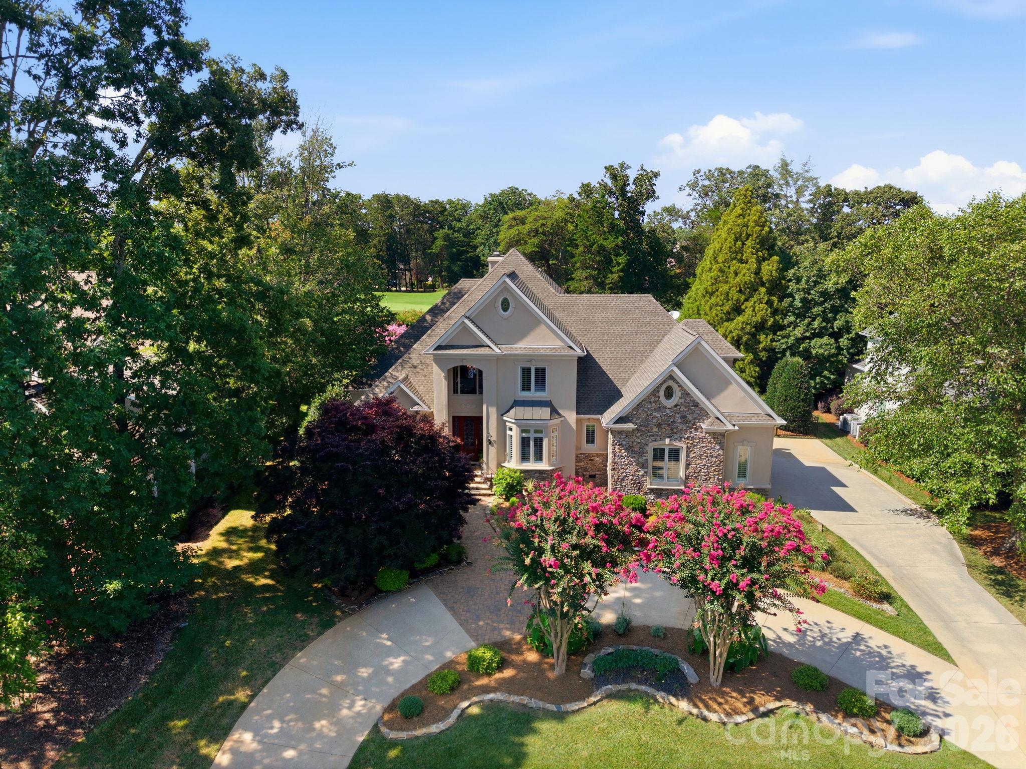 Aerial view of a stone-accented home framed by mature trees and pink flowering trees.