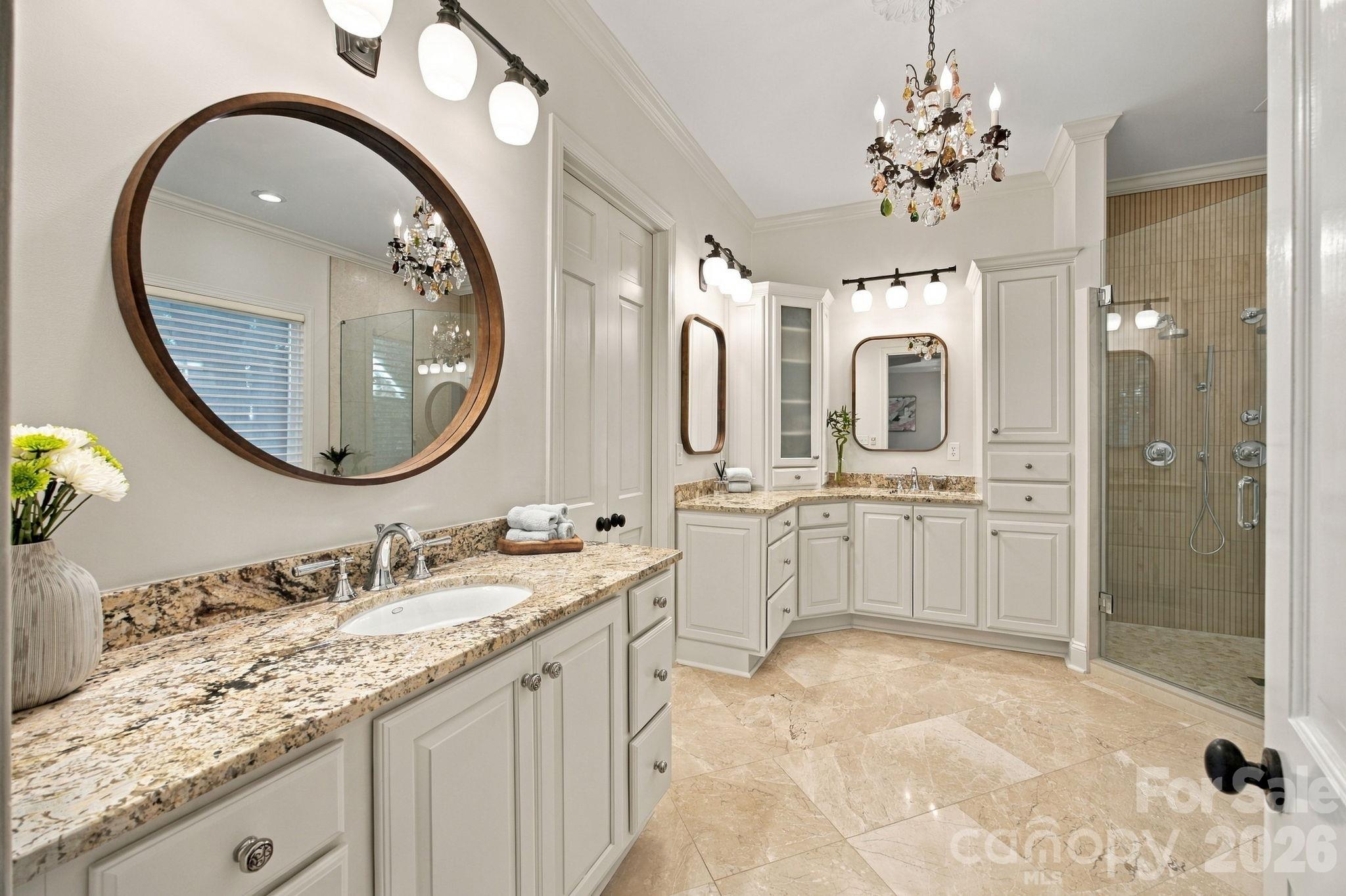 Primary bathroom with granite double vanities, large wood-framed mirrors, and a glass-enclosed shower.