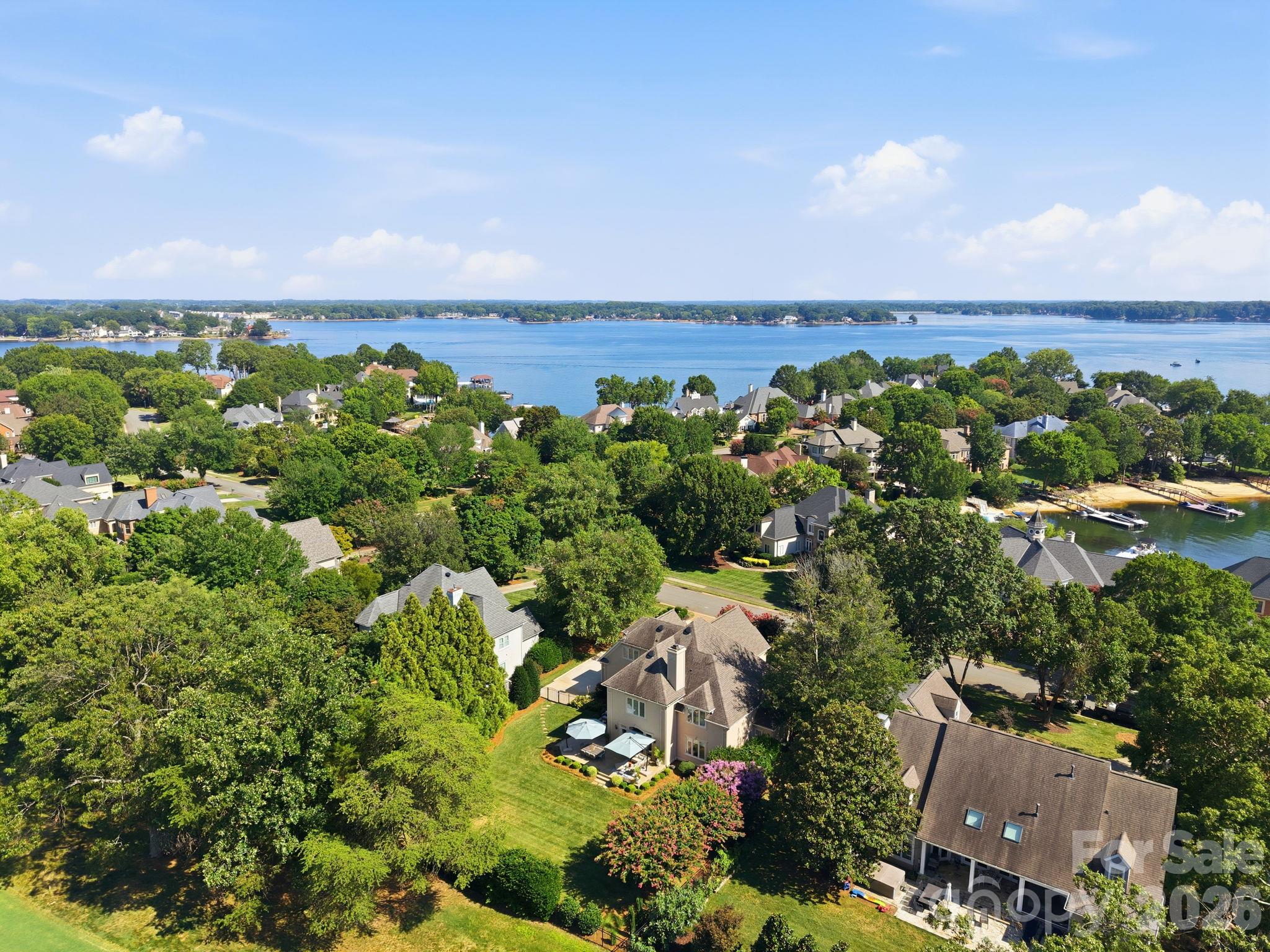 Lakeside home surrounded by trees, with an aerial view of the neighborhood and lake.