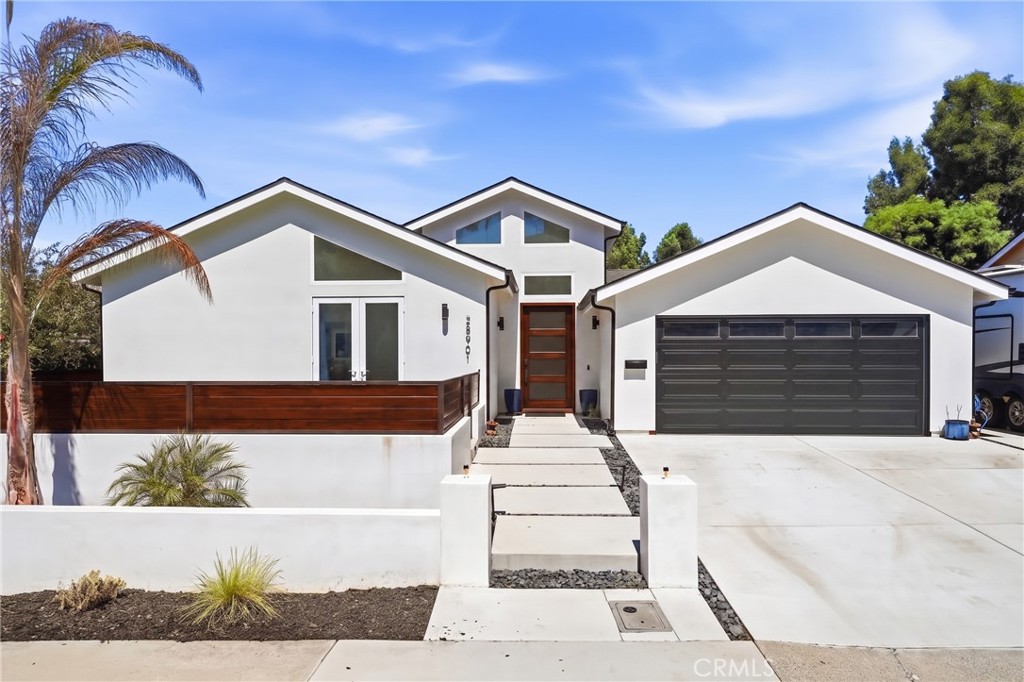 Modern white home with a wood-accented entry, dark garage door, and concrete walkway.