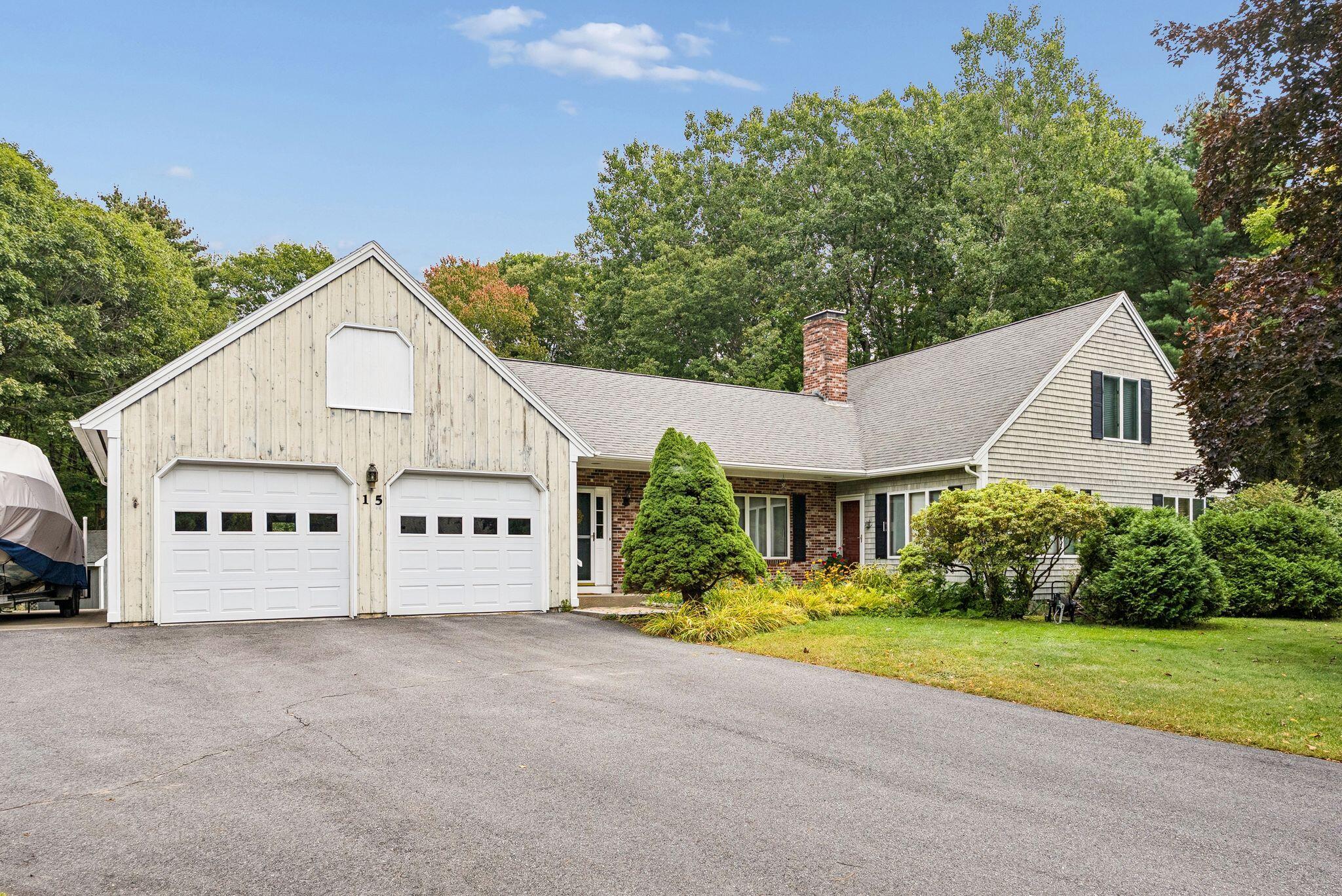 House exterior with two white garage doors, a brick chimney, and landscaped shrubs.