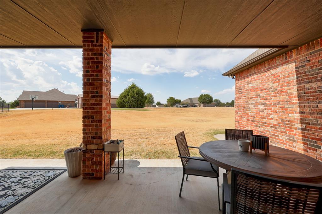 Covered brick patio with outdoor dining set overlooking a broad lawn and neighboring homes.