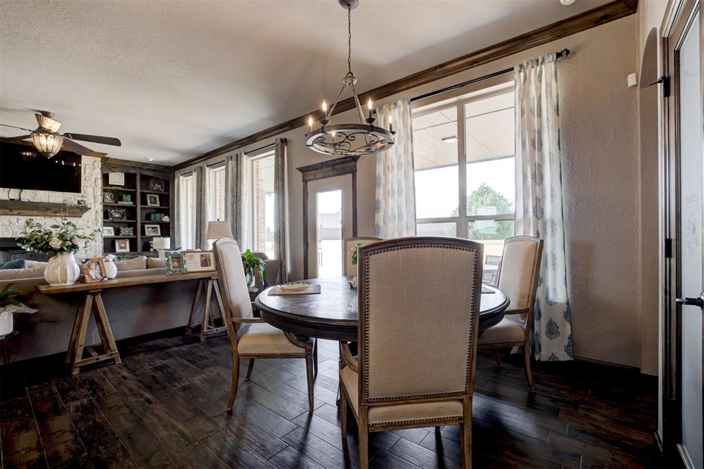 Dining area with a round wood table, upholstered chairs, large curtained windows, and dark wood floors.