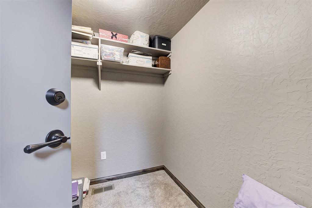 Storage closet with carpeted floor, high shelves, and boxes and containers.