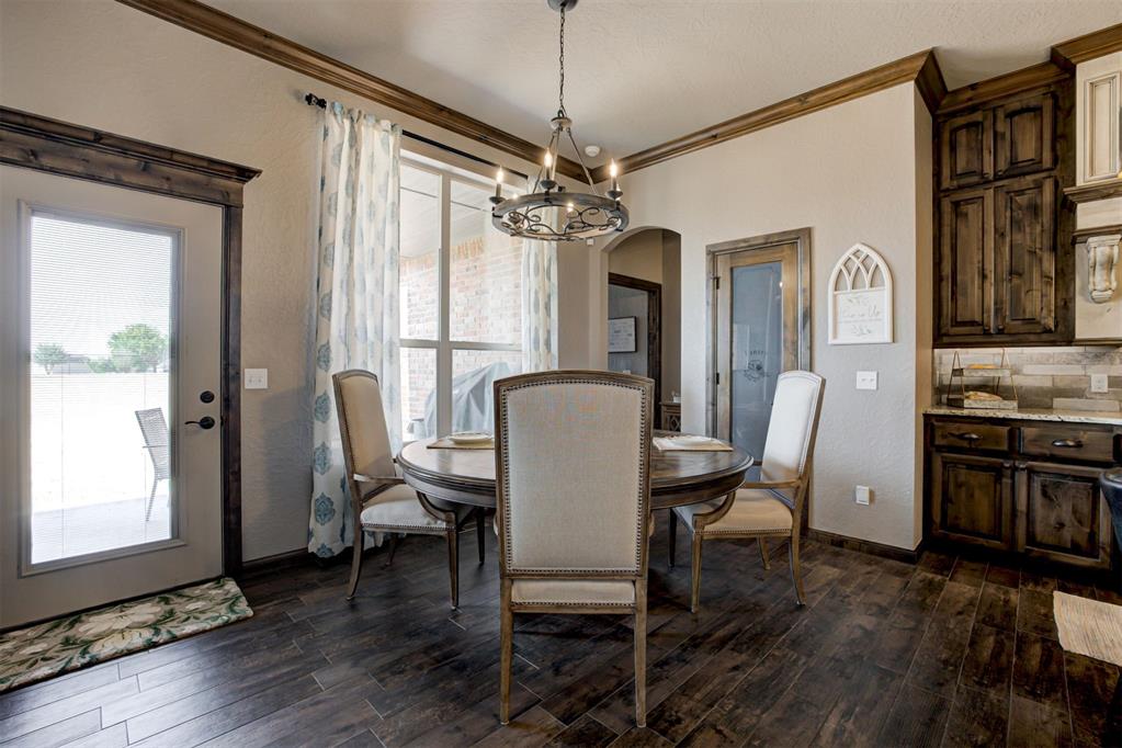 Dining area with a round table, upholstered chairs, chandelier, and adjoining dark wood kitchen.