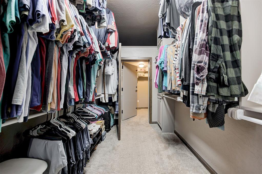 Walk-in closet lined with hanging clothes and lower shoe shelves, leading to an open doorway.