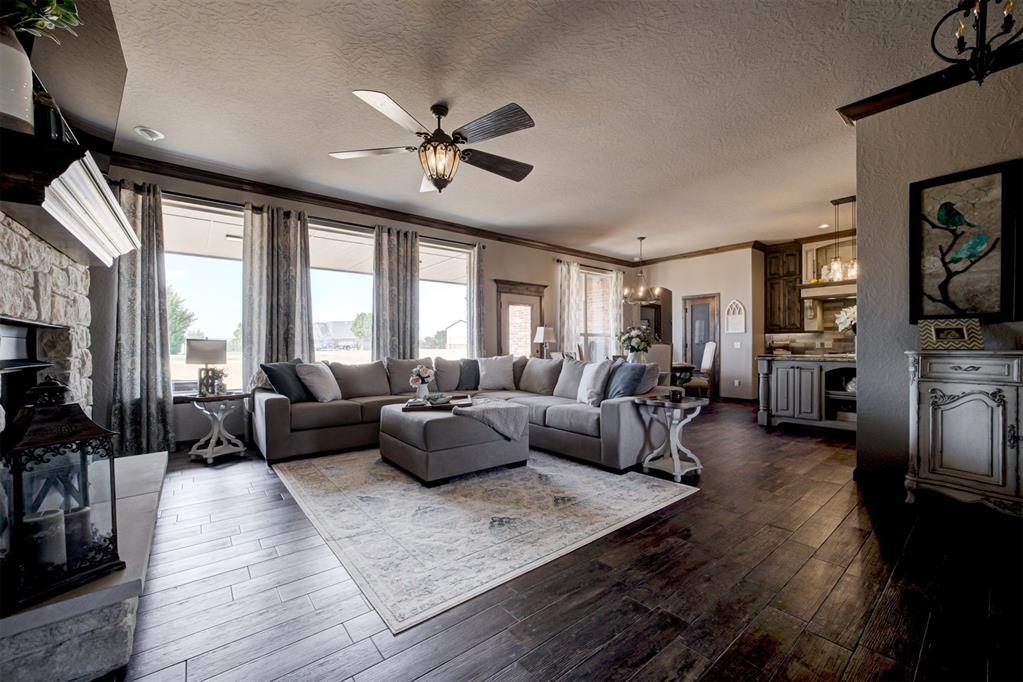 Living room with a gray sectional, stone fireplace, tall windows, and dark wood floors.
