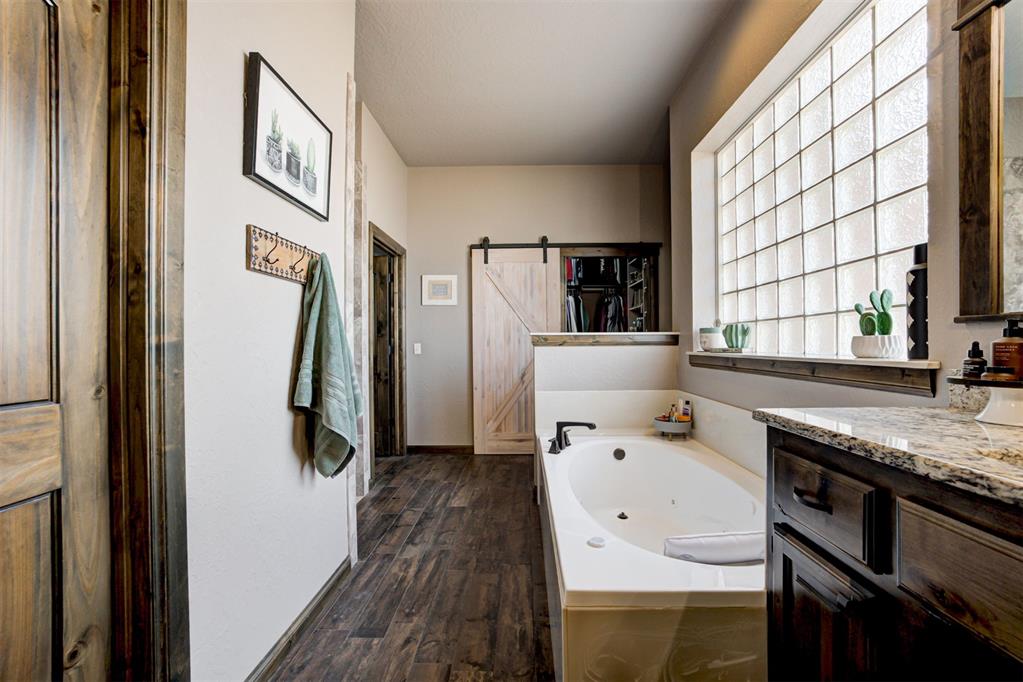 Bathroom with a soaking tub, granite vanity, glass-block window, and sliding barn door.