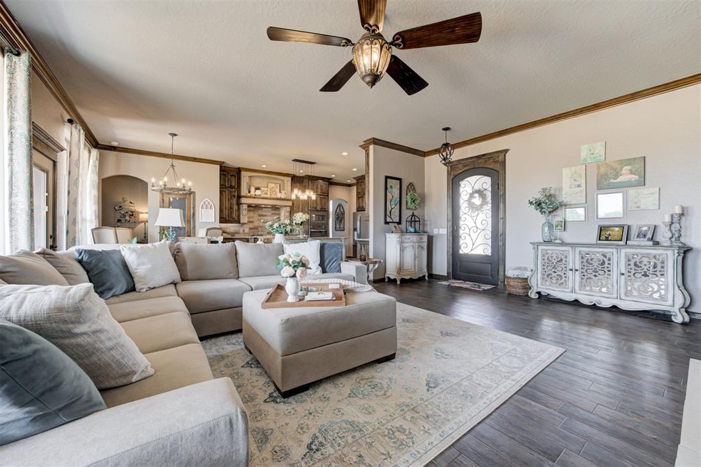 Living room with a large sectional, patterned rug, ceiling fan, and open kitchen.