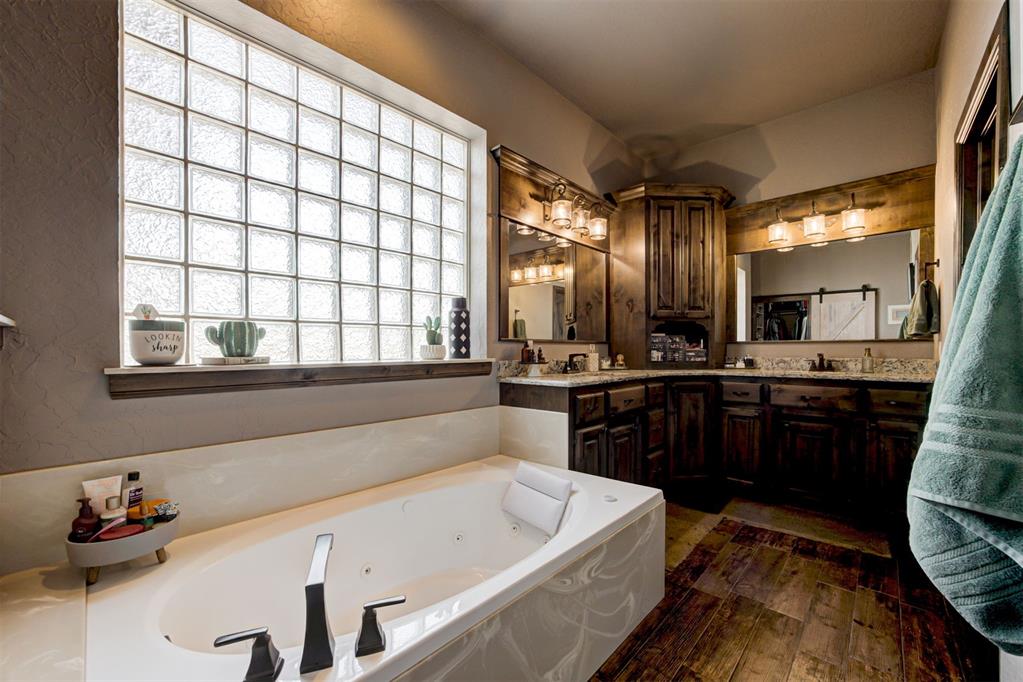 Bathroom with a jetted tub beneath a glass-block window and dark wood vanity.