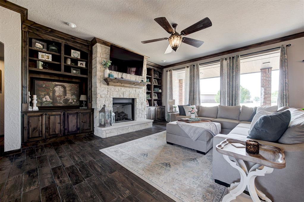 Living room with a stone fireplace, dark built-in cabinetry, and large curtained windows.